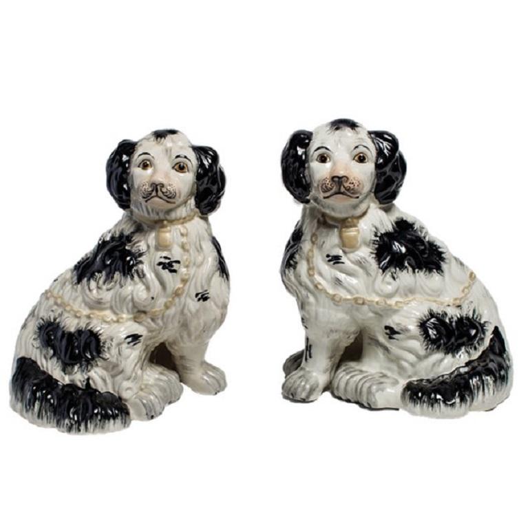 Handsome pair of porcelain black and white with gold collars Staffordshire dogs, made in England at the turn of the century. Due to its hand painted nature, each dog figurine has a distinct face with expressive eyes and muzzle. The seated dogs each