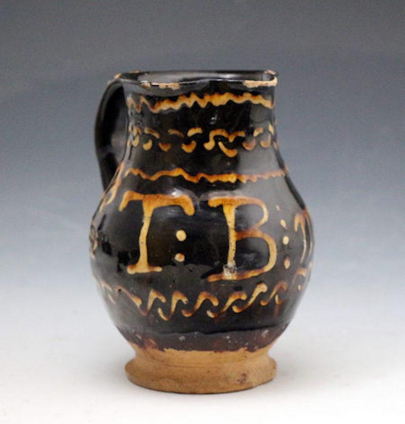 Dated: 1816 Staffordshire, England

A slipware earthenware pitcher with a dark brown ground with dark honey-colored trailing slip decoration with the initials T:B and the date 30 March 1816. Staffordshire pottery, England.

Dimensions: 5.5