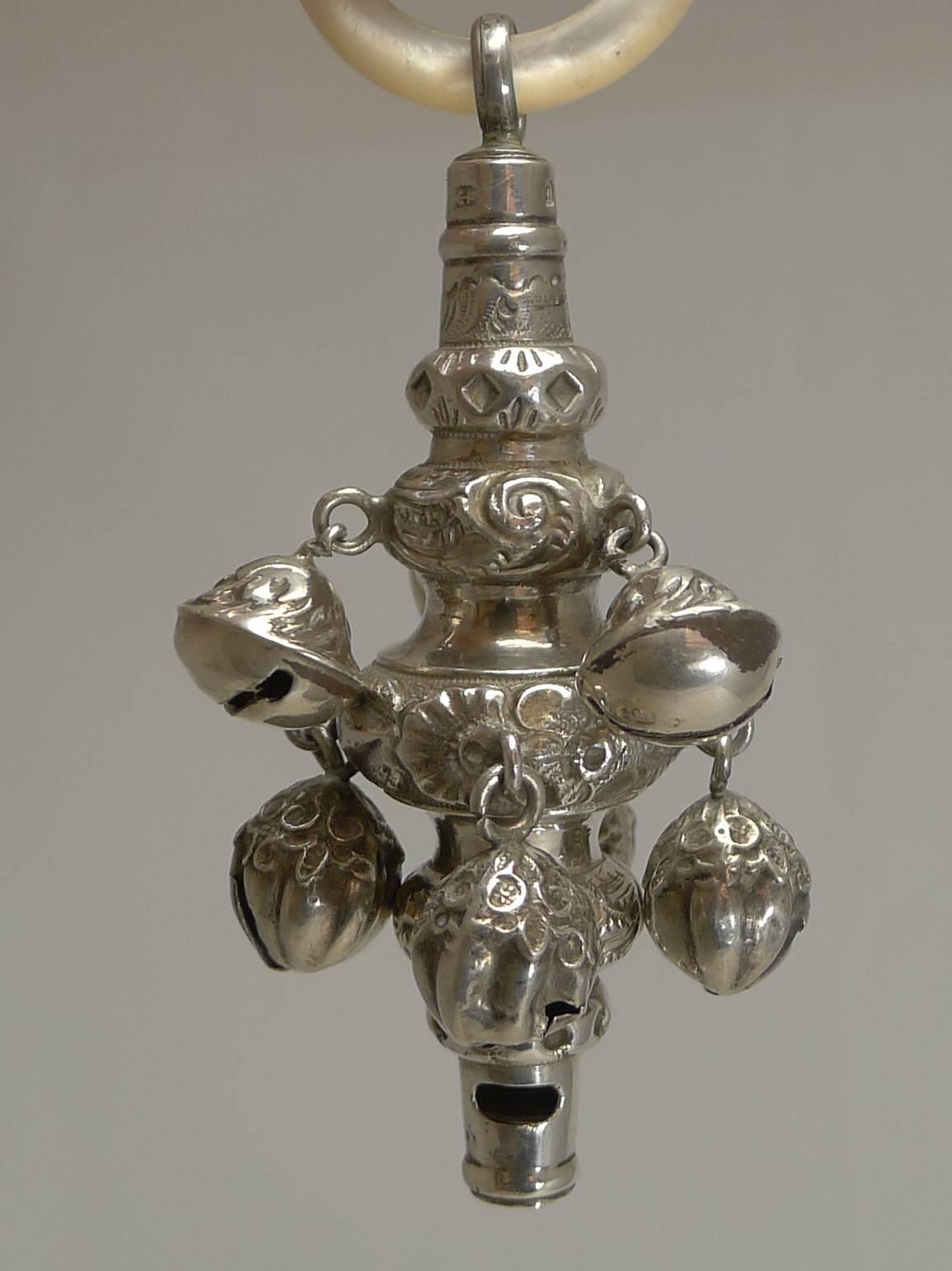 A beautiful English Victorian combined baby's rattle with an integral whistle, having eight bells and a mother-of-pearl teething ring.

All made from English sterling silver with repousse or embossed decoration and fully hallmarked for Birmingham