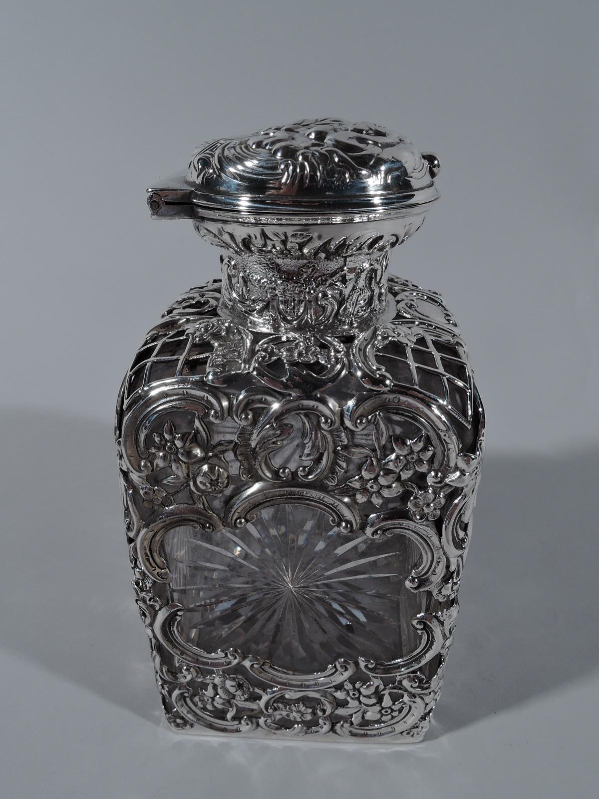 Edwardian Rococo clear glass perfume in sterling silver cage. Made by William Comyns in London in 1903. Rectilinear with short neck. Sterling silver cage with open multifoils revealing cut-stars, and pierced flowers, scrolls, and diaper. Short neck