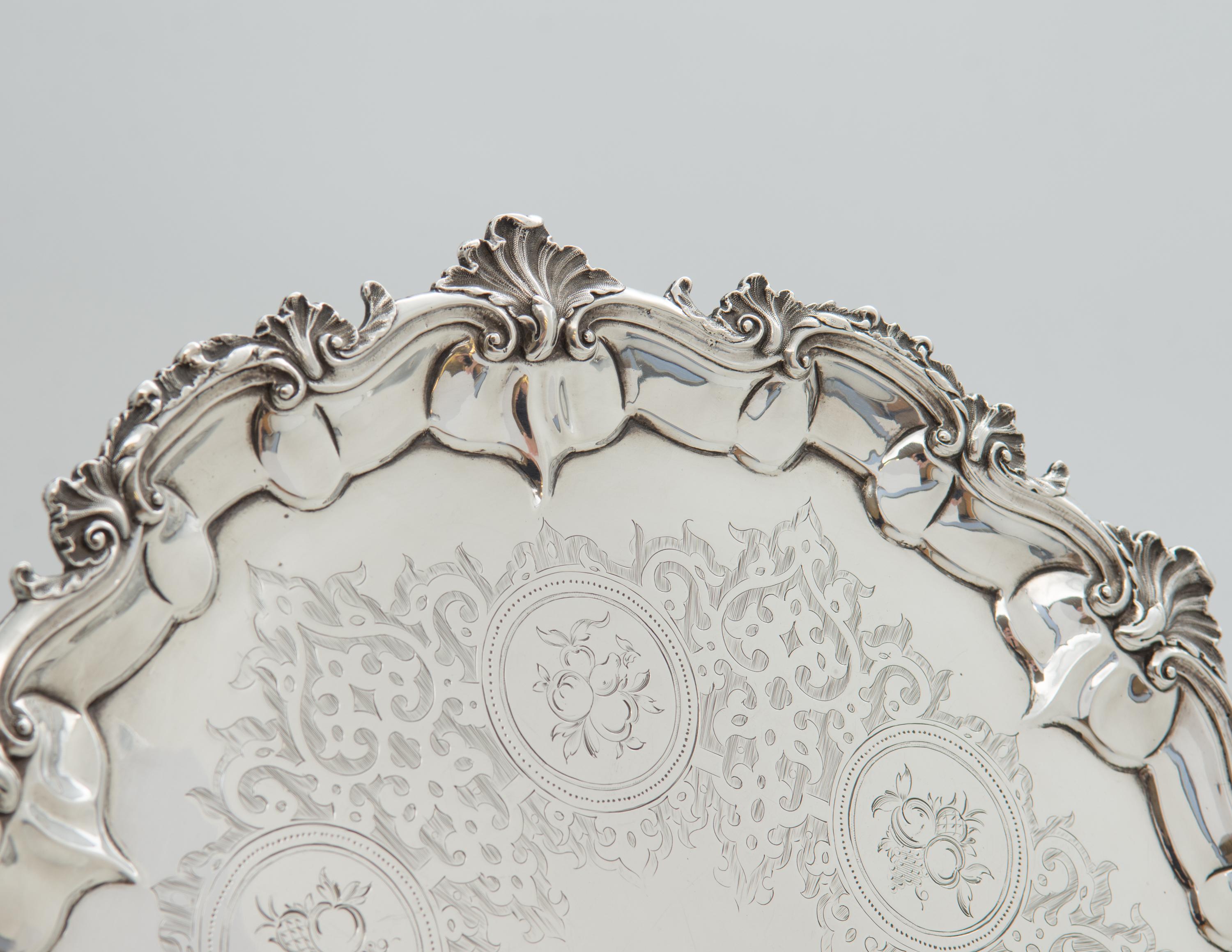 Antique Victorian sterling silver salver, hallmarked in London by Robert Harper in 1859.

The salver has a pie crust edge with scroll and shell border, raised on three cast scrolled feet. The field is beautifully hand engraved, depicting various