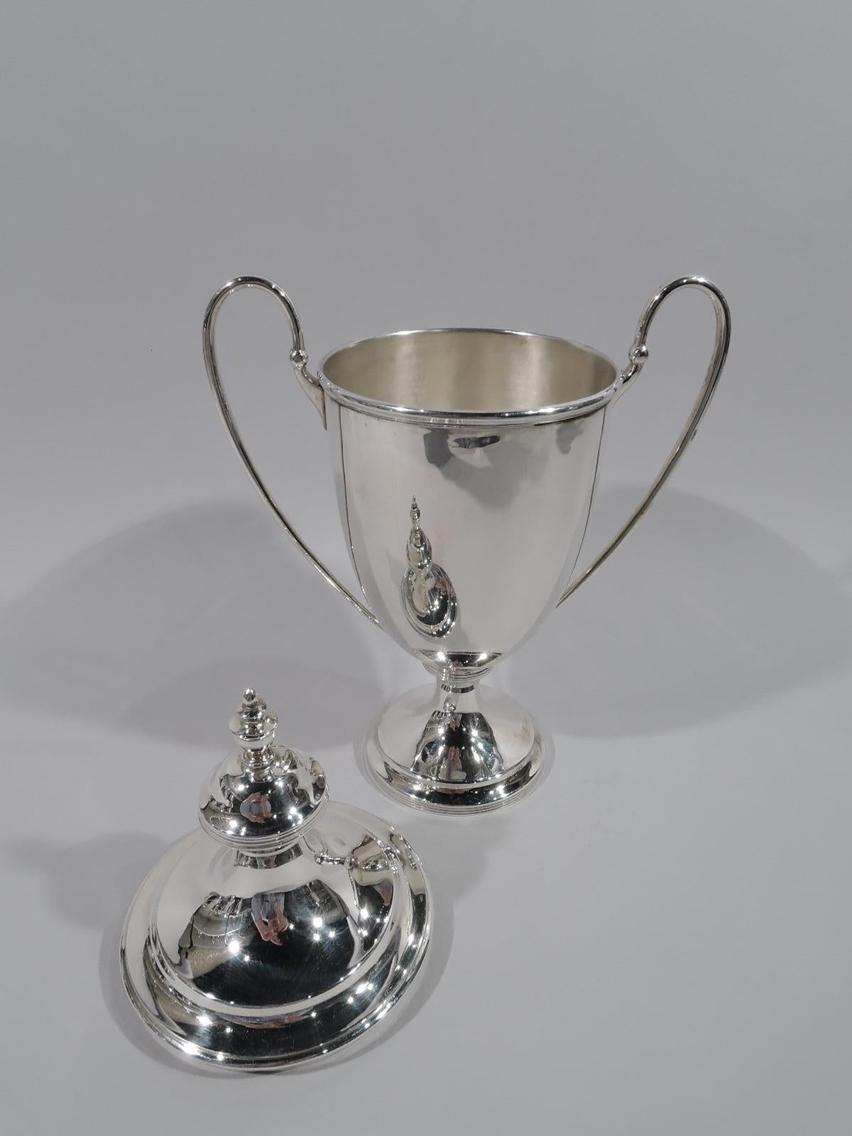 Victorian sterling silver trophy cup. Made by Daniel & John Wellby in London in 1893. Amphora urn with high-looping side handles and stepped foot. Double-domed cover with self-referencing vase-finial. Reeding. A very nice understated winner’s cup.