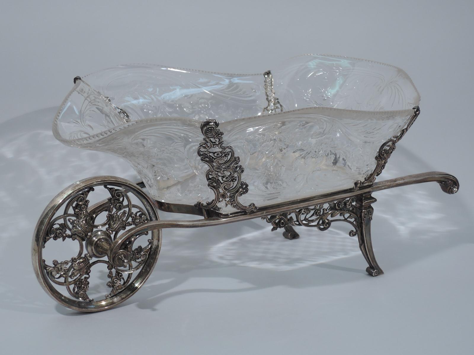 Edwardian sterling silver and crystal wheelbarrow. Made by William Comyns in London in 1907.

Shaped rectangular crystal bowl with cut flowers and leaves. Bowl set in sterling silver frame with two stretchers terminating in volute scrolls, front