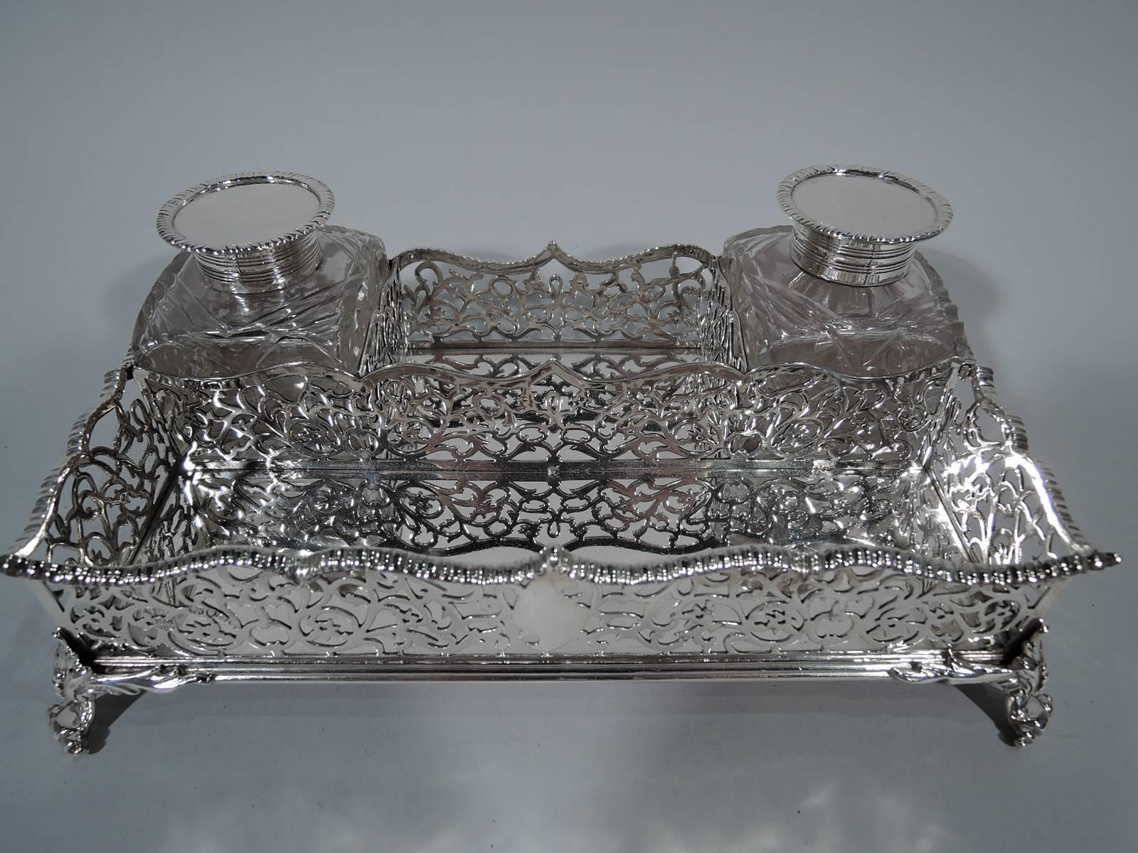 Victorian sterling silver stand with two inkpots. Made by William Gibson & John Langman in London in 1889. Stand is rectangular with solid well and four leaf-mounted volute-scroll supports. Sides are pierced scrollwork and rim is notched and wavy