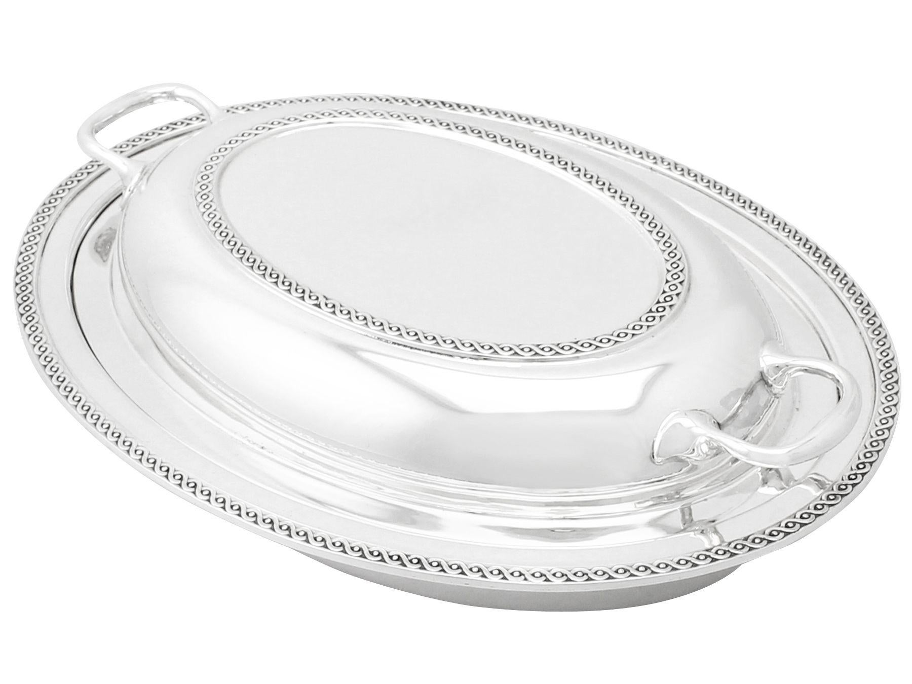 An exceptional, fine and impressive antique George V English sterling silver entree dish; an addition to our ornamental dining silverware collection.

This impressive antique George V sterling silver entree dish has a plain oval rounded