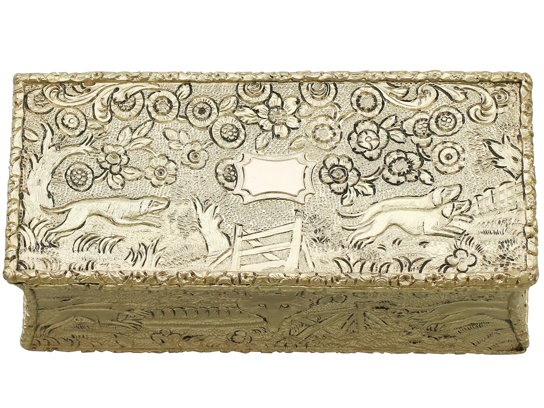 This exceptional antique George IV sterling silver gilt Snuff box has a rectangular waisted form.

The surface of this antique silver box is embellished with exceptional chased decoration depicting hunting hounds chasing a fox in an rural