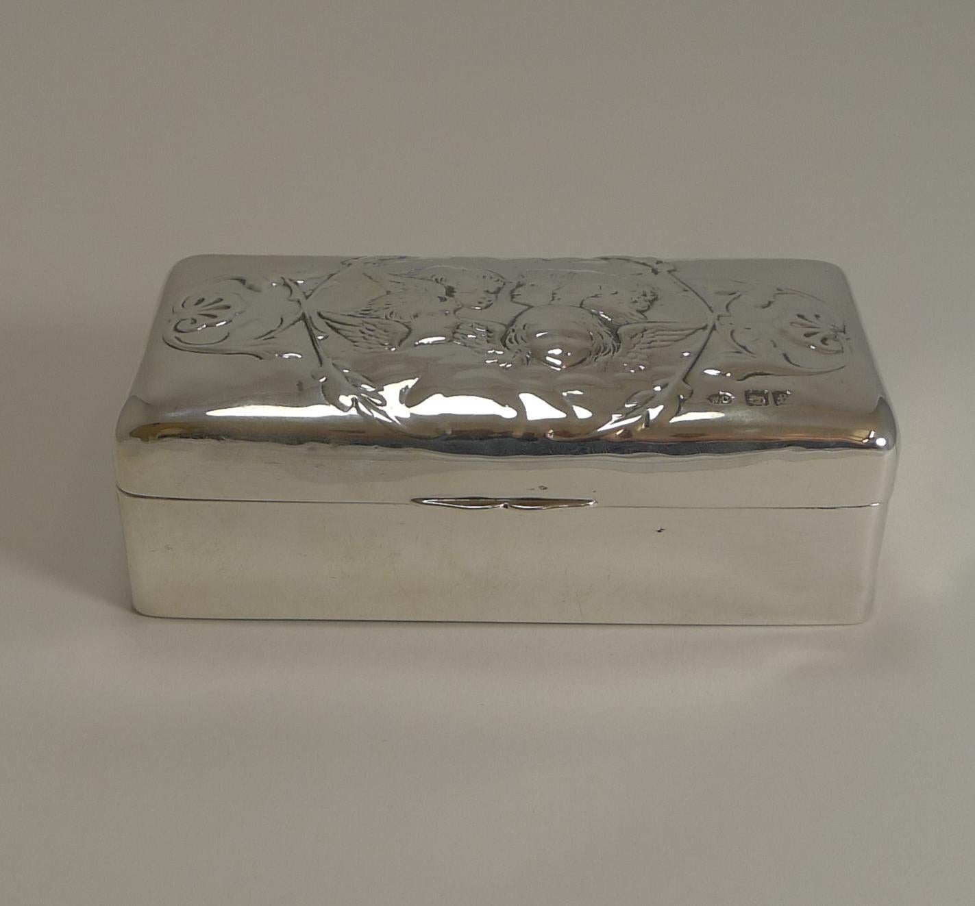 A wonderful solid box made from English sterling silver featuring the famous five winged Cherubs to the lid.

The hinged lid fits well and once opened, reveals a navy blue velvet and silk lining.

The box is fully hallmarked for London 1901