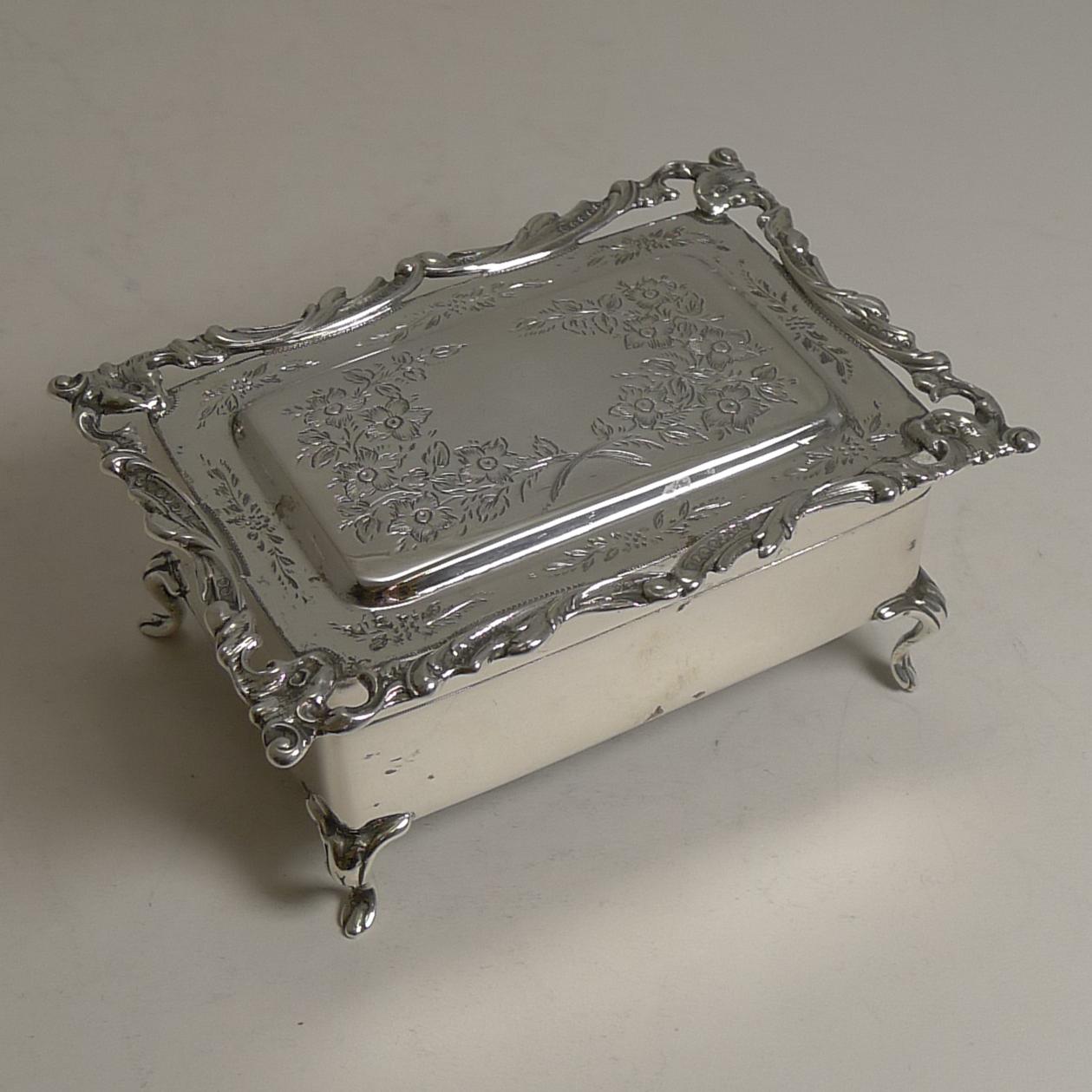 A stunning antique English sterling silver jewelry box standing on four very elegant legs.

The hinged lid is engraved with two sprays of floral and foliate bouquets creating a vacant cartouche to the centre. The border of the lid is made with a