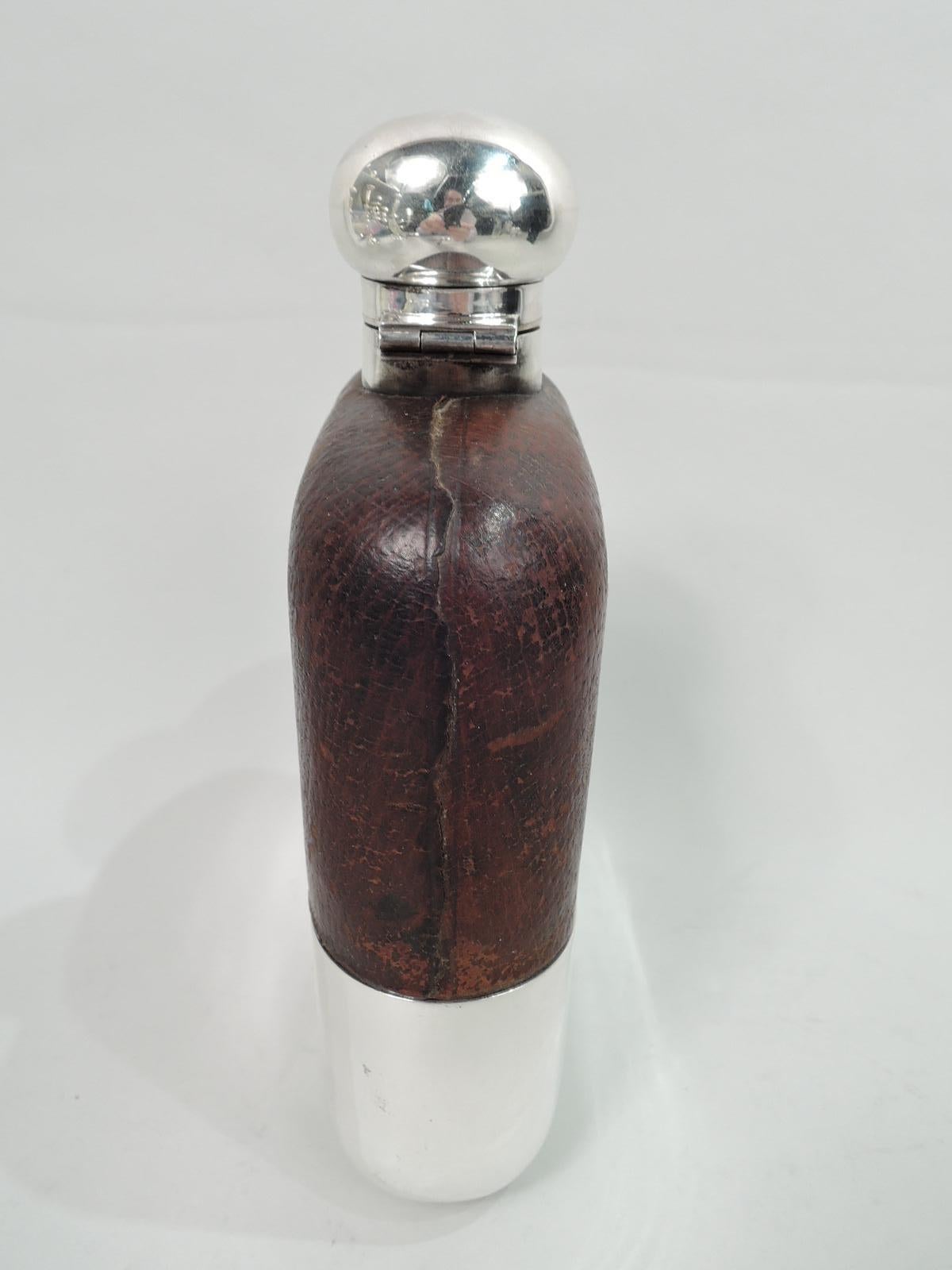 George V safari flask. Made by James Dixon & Sons in Sheffield in 1927. Clear glass body. Top half encased in leather with cutout tubular windows. Bottom half has detachable sterling silver cup. Short straight sterling silver neck with hinged and