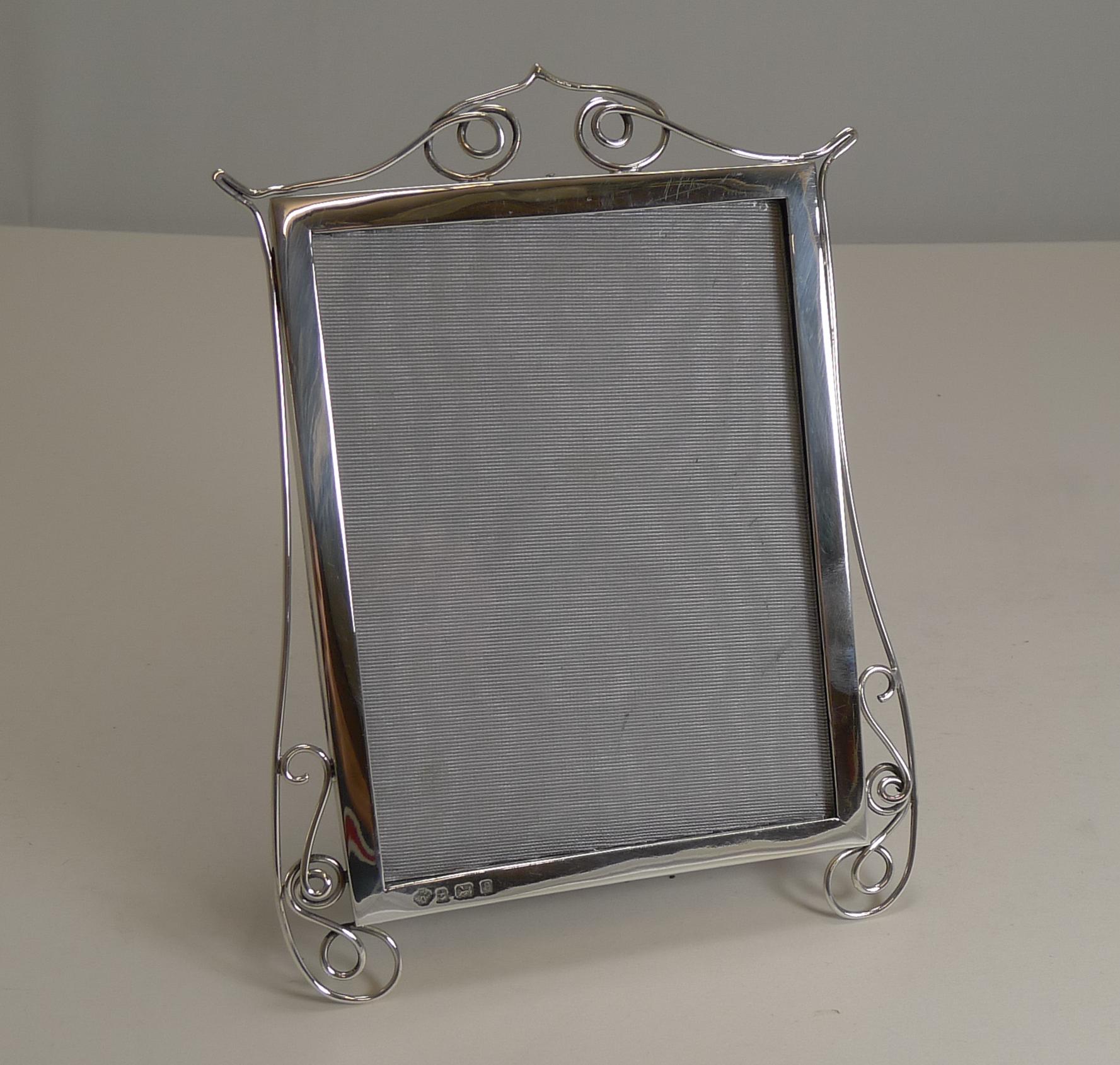 A wonderfully decorative and unusual Edwardian sterling silver frame by the top-notch silversmith, William Hutton and Sons.

The simple frame is decorated with sterling silver wire-work, creating two legs.

The back has a leather backing