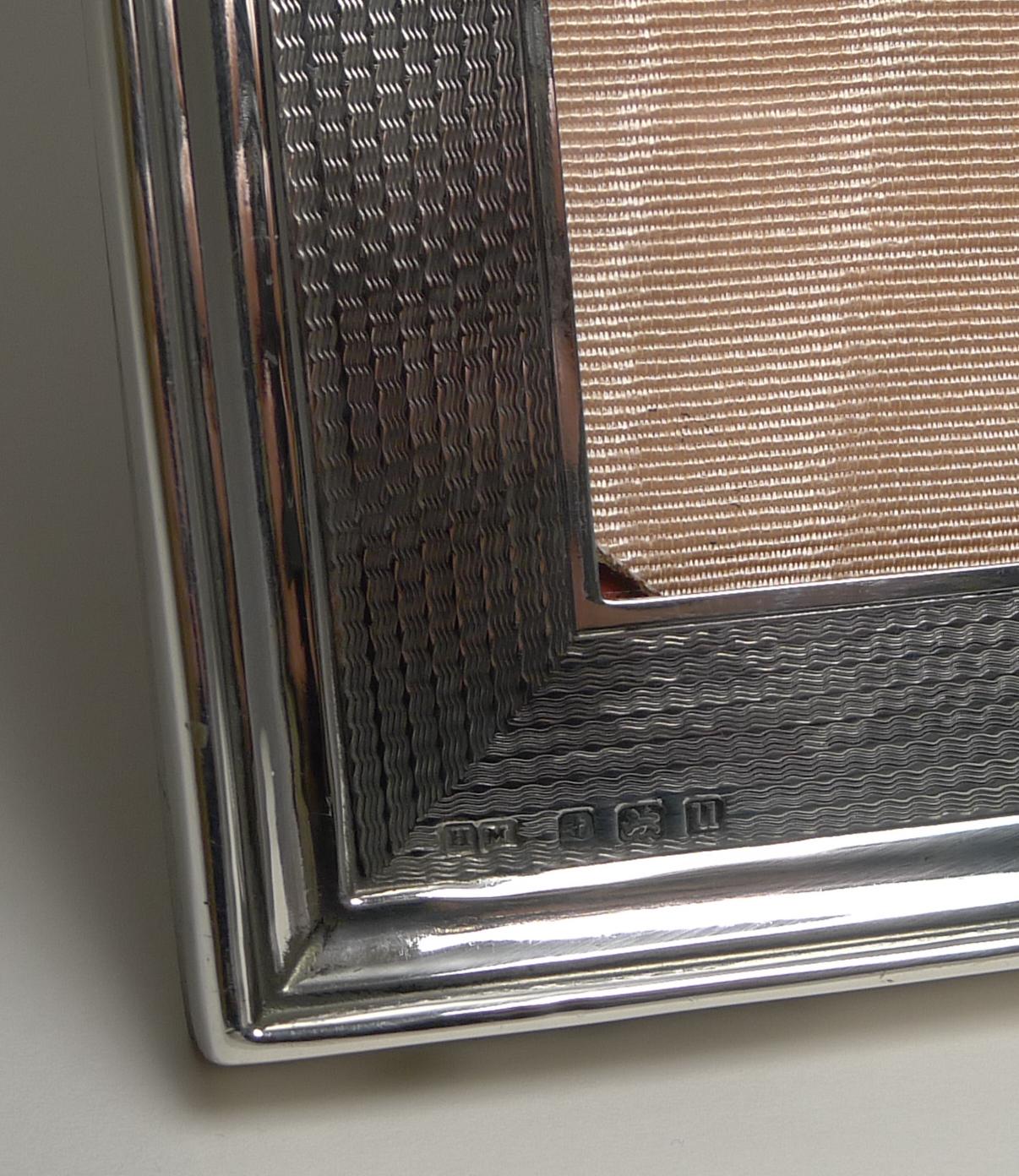 A handsome antique English photo frame made from sterling silver with an engine turned decoration and a lovely shaped top. To the top of the silver is a small circular vacant cartouche.

The backing incorporates a folding easel stand, all made
