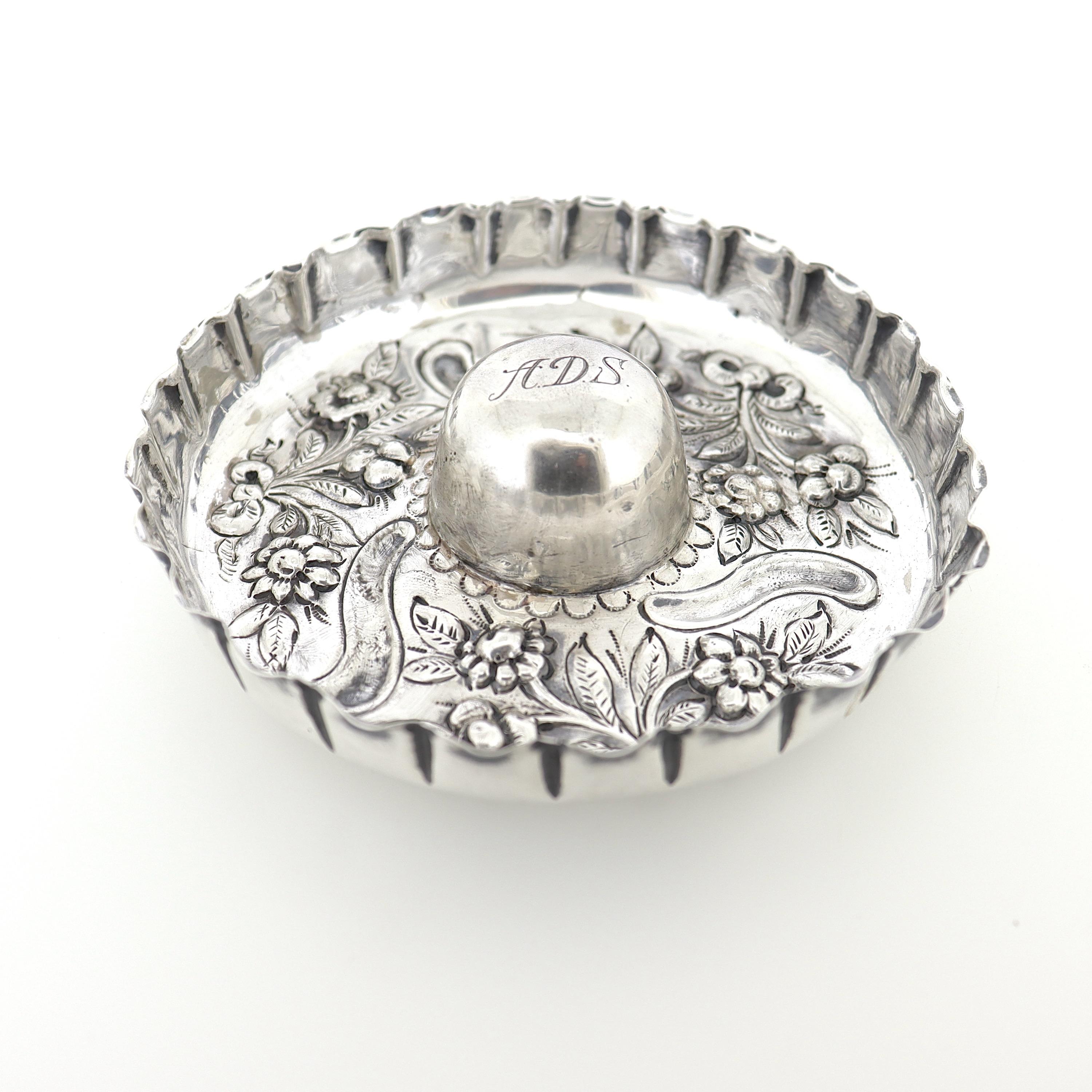 A fine antique English sterling silver ring stand.

By William Comyns. 

With a scalloped edge and repousse floral designs.

The ring nub is monogrammed 