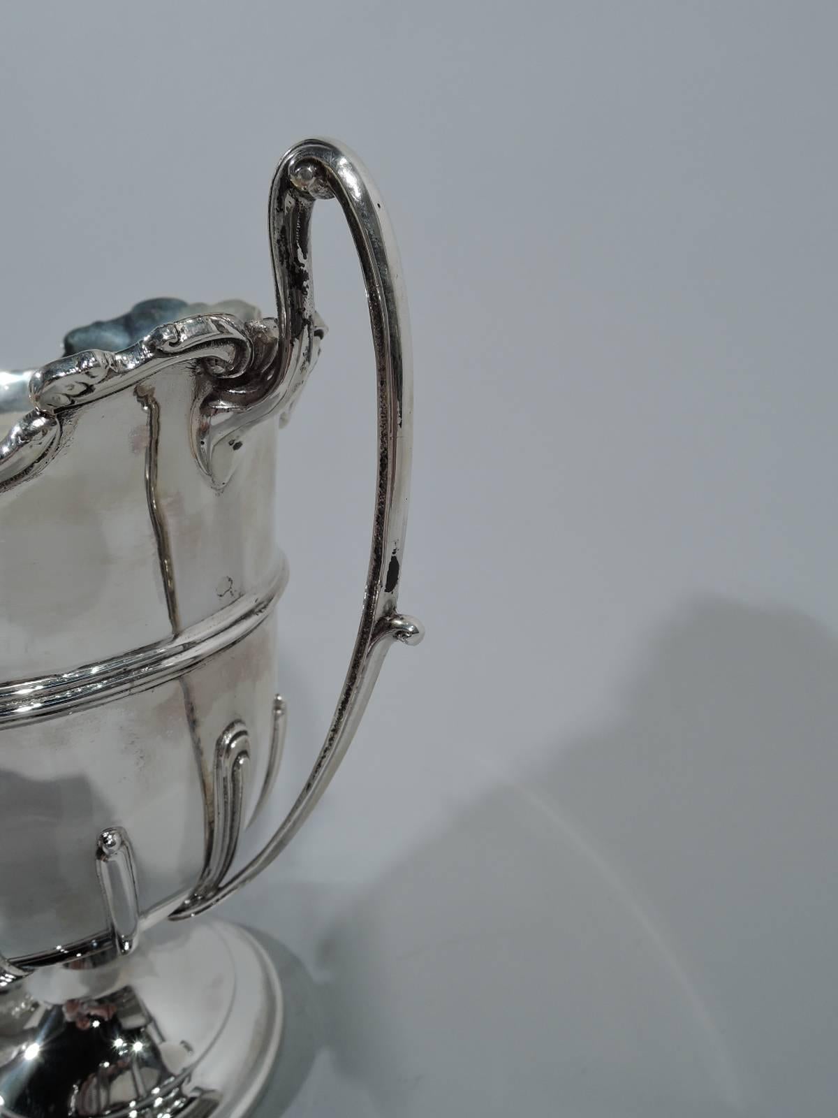 George V sterling silver trophy cup. Made in Birmingham in 1929. Bowl has curved bottom on stepped foot and high-looping scroll side handles. Irregular flared rim with scrolls. Applied girdle and gadroons. Fully marked (maker’s stamp includes