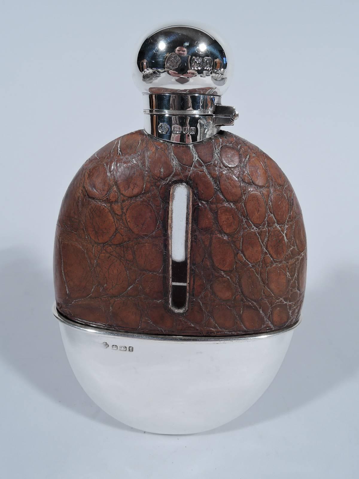 Victorian safari flask. Made by William Hutton & Sons in England. Clear glass with detachable sterling silver cup and short neck with hinged cork-lined cover. Top encased in brown leather with cut-out tubular windows. Wide body suitable for a large