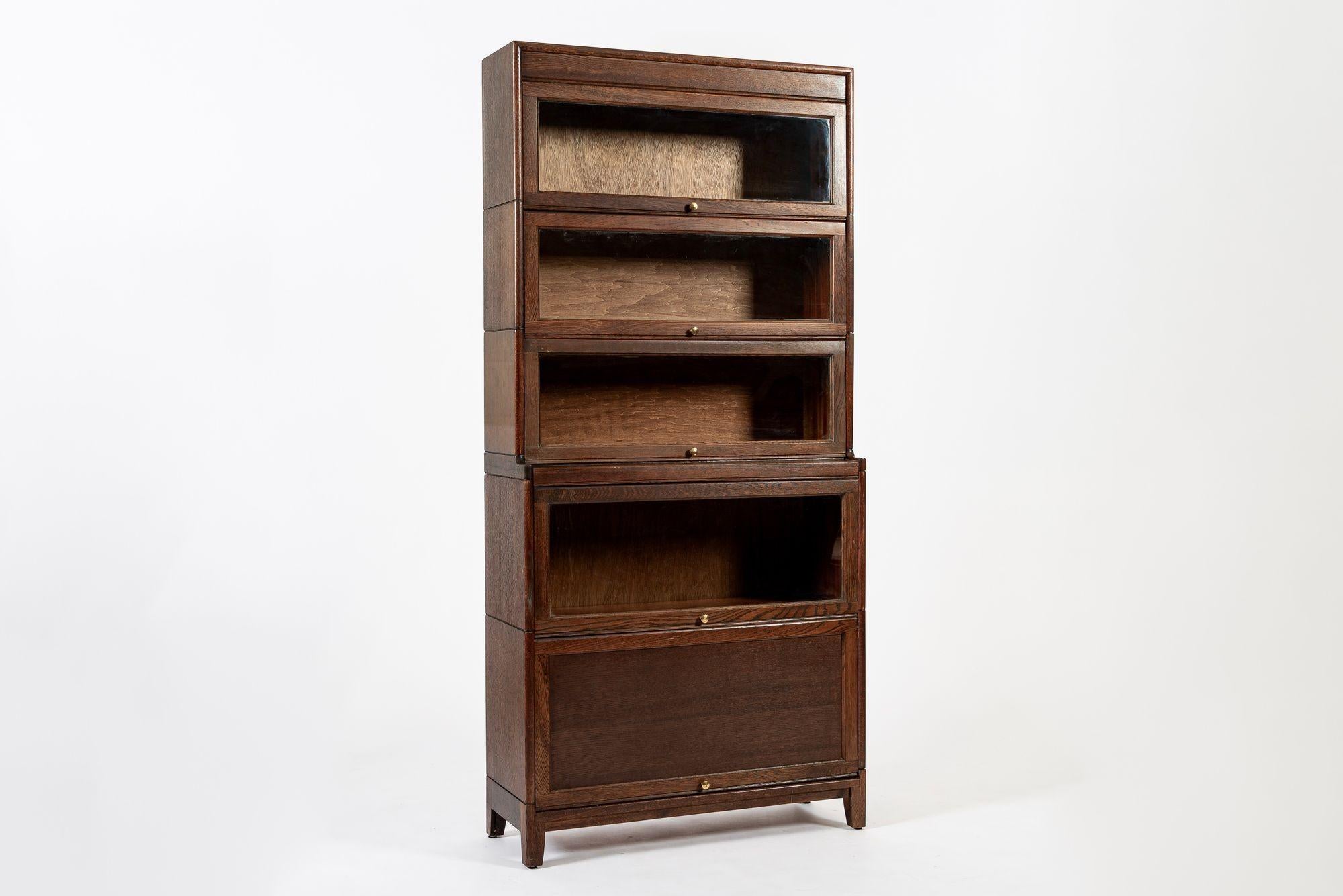 Questo antico mobile libreria in legno per avvocati o barrister in stile mission inglese a cinque ripiani risale ai primi anni del 1900. Realizzata a mano in legno di quercia bianca, questa libreria alta e modulare ha un formato unico con tre