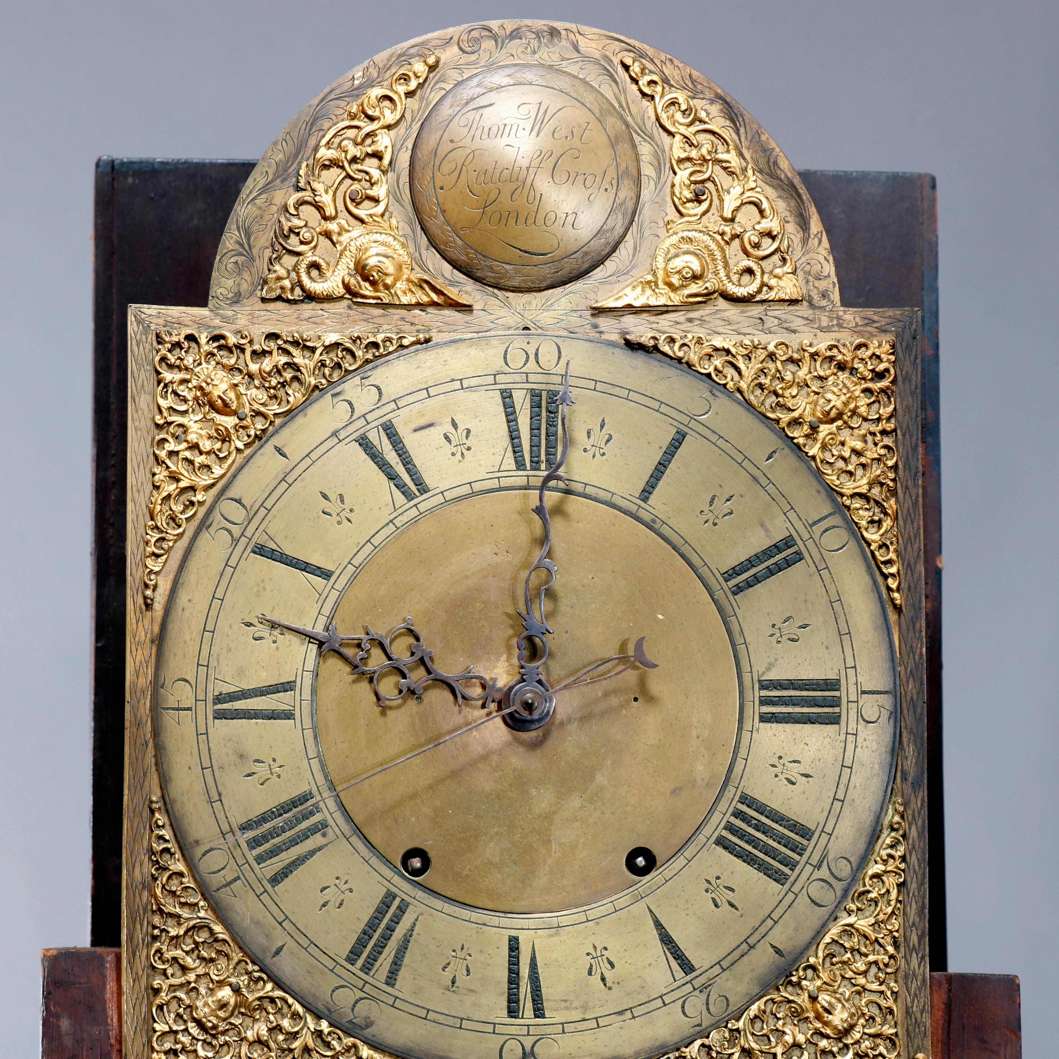 An antique English long case clock by Thomas West for Radcliff Bros, London offers flame mahogany case with broken arch top having finials surmounting hood with reeded and columns and satinwood inlaid base raised on splayed feet; cast face with