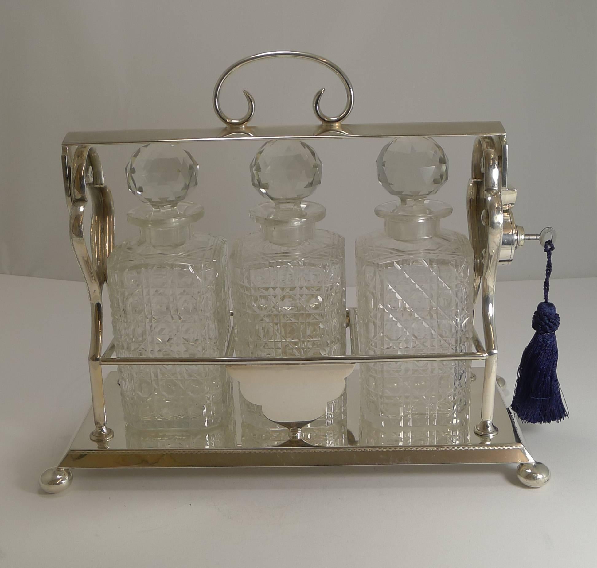A handsome antique English three decanter Tantalus with silver plated frame and standing on four bun feet.

The working key requires a clockwise turn, the lock barrel is then pushed down to release the bar covering the stoppers. The bar then snaps