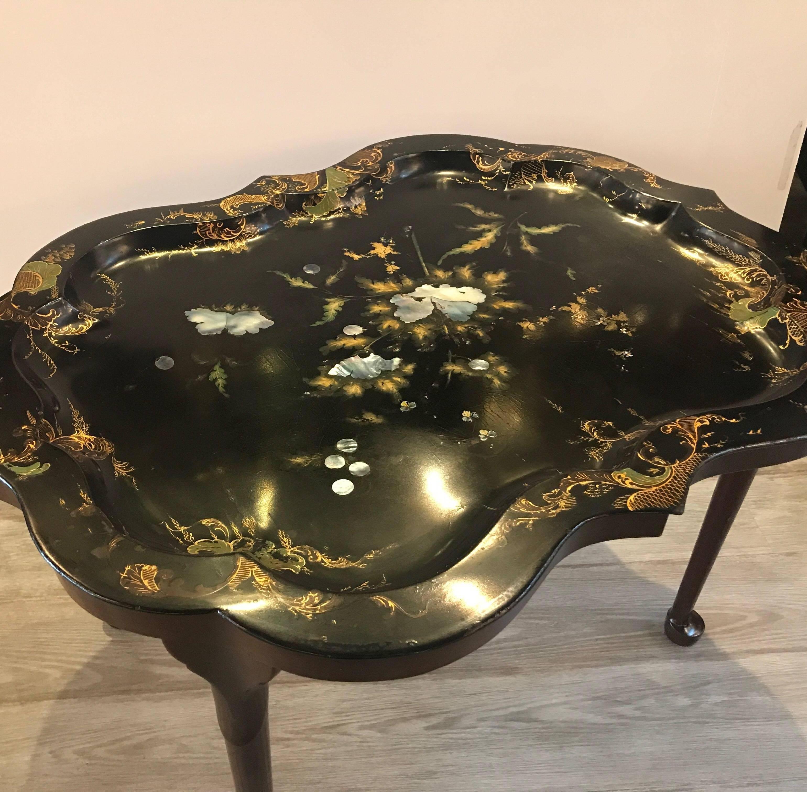 An English tole ware tray table with mother of pearl inlay. The black background with hand painted and gilt decoration with mother of pearl inlay in a floral design. The custom made mahogany base with tapering legs resting on spoon feet. The tray is