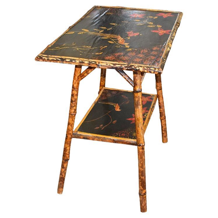 A traditional English burnt bamboo side table. This multi-level side table features two shelves, each japanned with a black, yellow, and red bird motif. The top tier is a large rectangular shape and has a border of bamboo around the edges. The legs