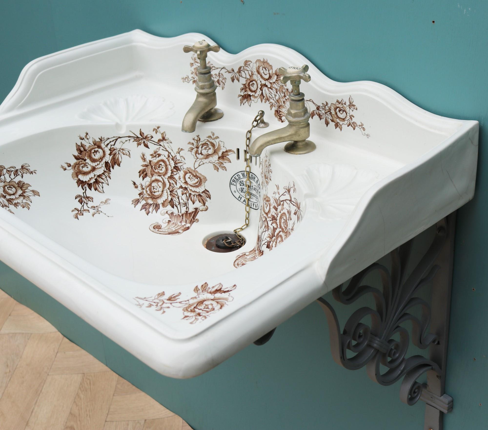 An antique transfer printed basin depicting floral scenes manufactured by Fred Walsh and Co. Supplied with wrought iron wall mounted brackets. Original nickel plated taps.