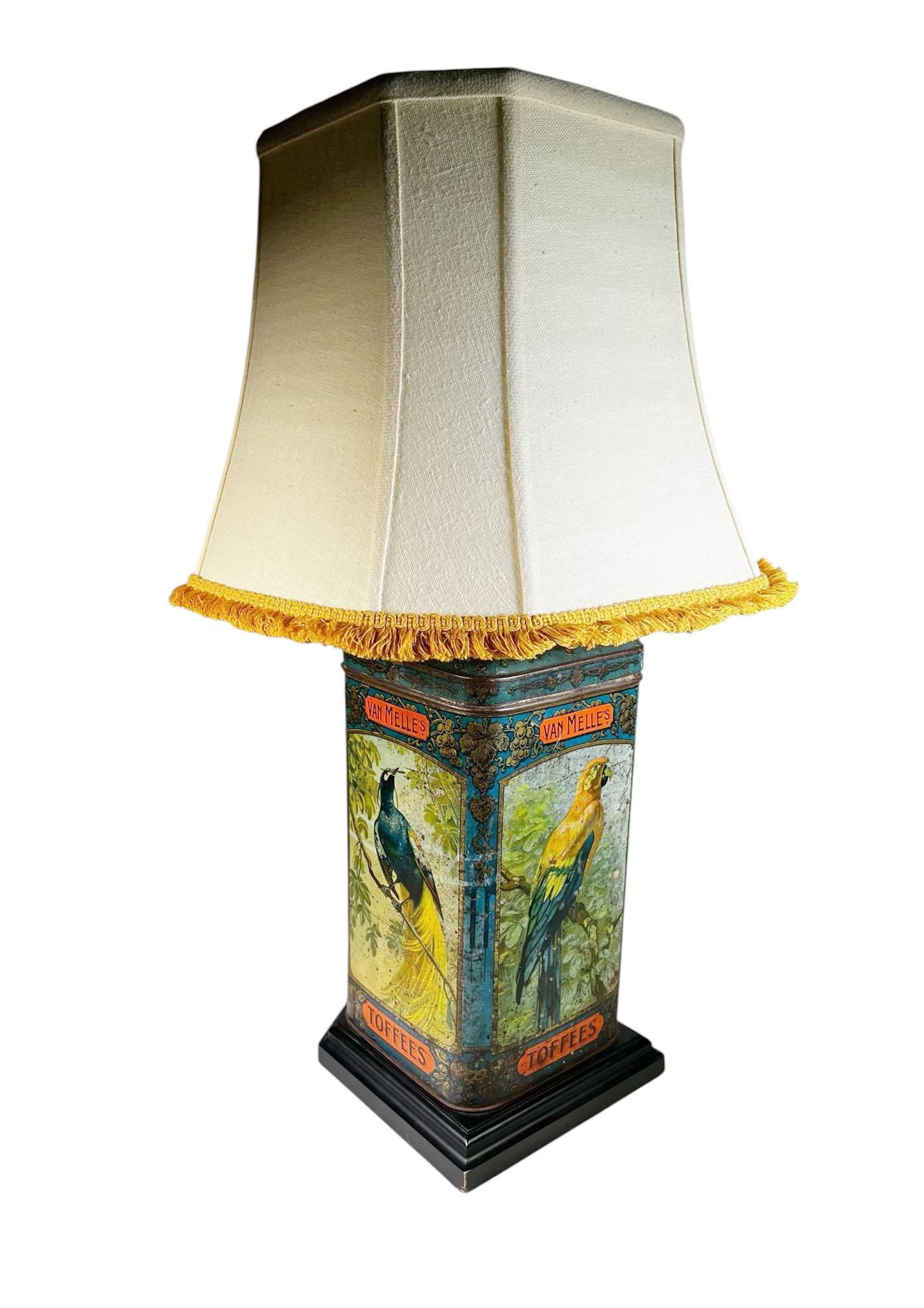 A rare and whimsical treasure this antique English Van Melle's Toffees tin has been beautifully repurposed as a table lamp, complete with a complementary shade. The tin is richly hand painted with an exotic array of birds, including parrots and