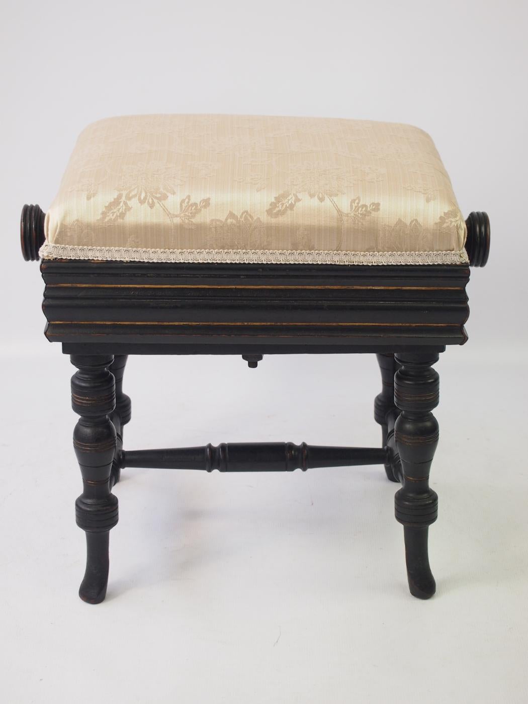 An attractive antique Victorian Aesthetic Movement piano stool with rise and fall action operated by turning knobs on either side of the seat dating from circa 1880. It has a reeded seat support and knobs and stands on turned legs with cross