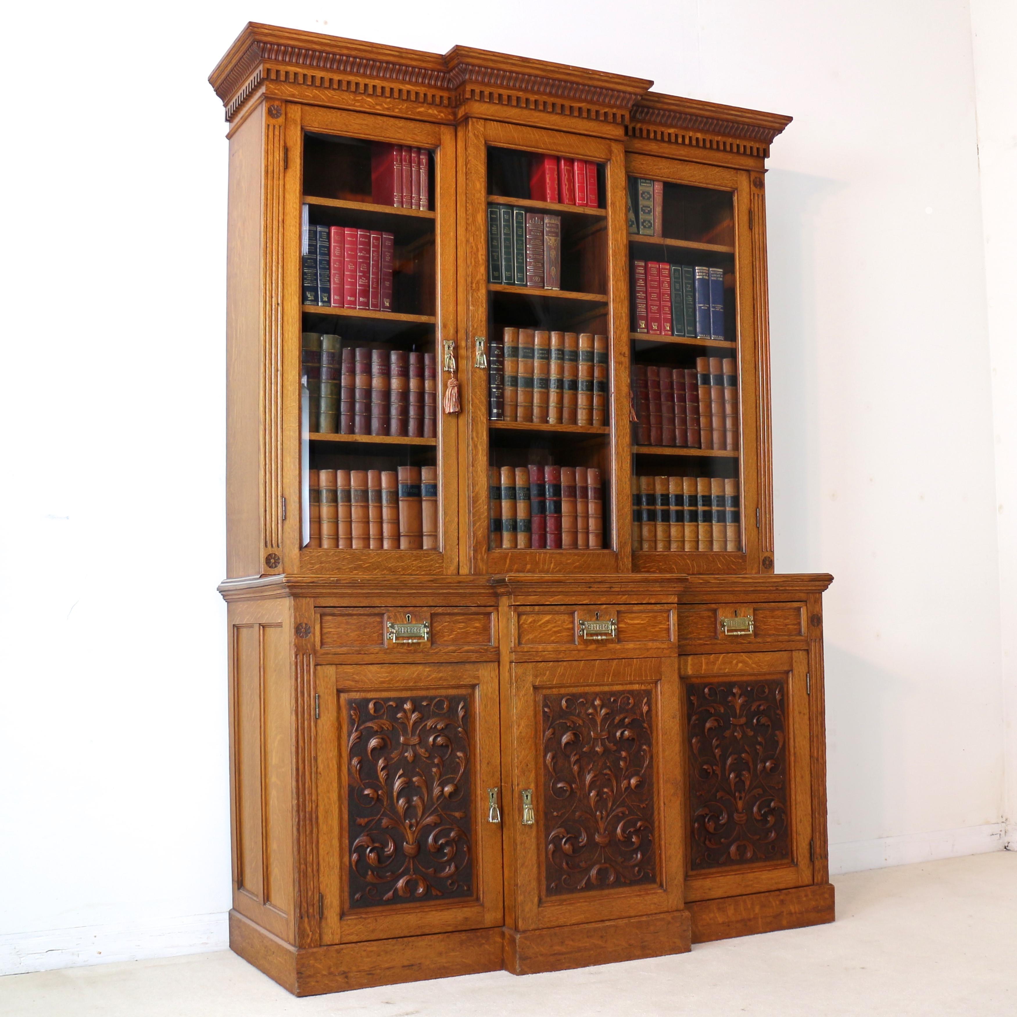 A beautiful Victorian three door breakfront bookcase or display cabinet attributed to Maple & Co and in the Art Nouveau/Arts & Crafts taste. In golden quarter-sawn oak with bevelled glass panes to the glazed doors it features a reeded and dentil