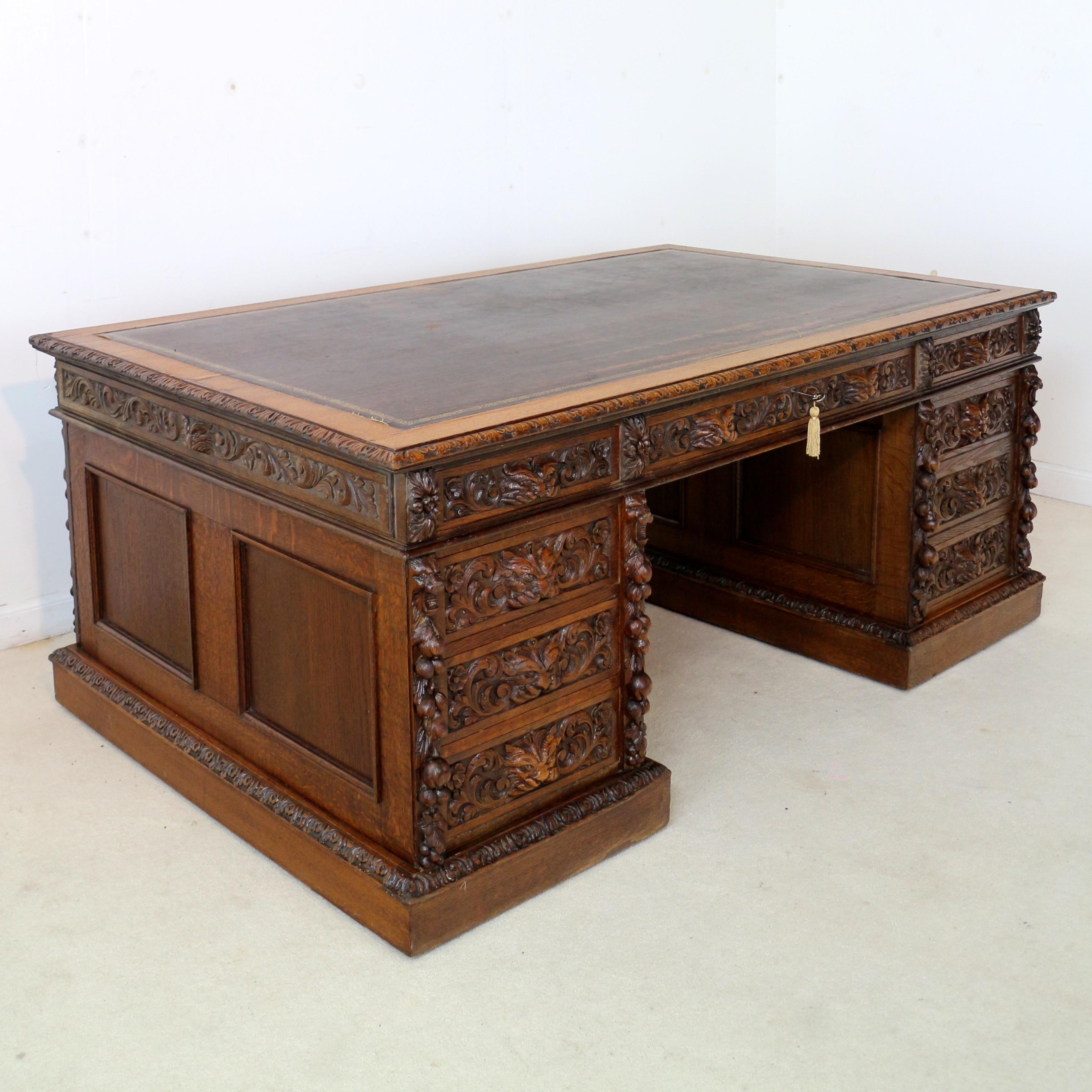 A stunning, beautifully carved Elizabethan Revival Victorian oak partners desk attributed to Edwards & Roberts of London. The rectangular top with a foliate carved edge and gilt embossed brown faux leather writing surface above a carved frieze. One