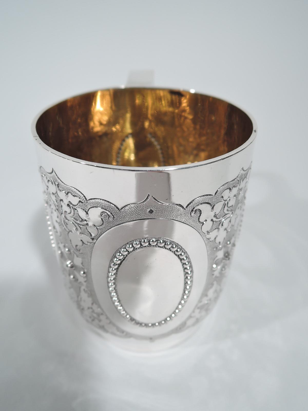Victorian sterling silver baby cup. Made by Daniel & Charles Houle in London in 1857. Upward tapering sides, swooping s-scroll handle with heart terminal, and short foot. Beaded oval rings (vacant) surrounded by stylized leaves and flowers on