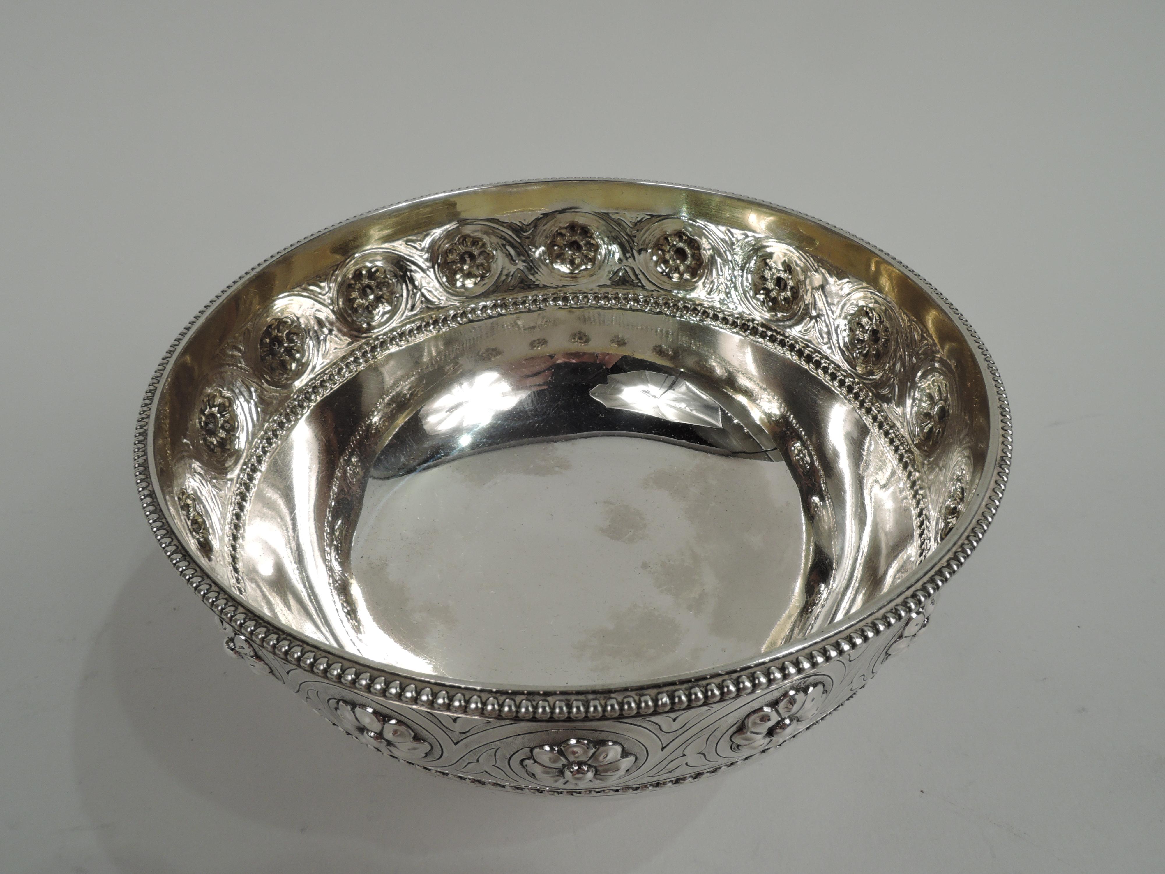 Victorian Classical sterling silver bowl. Made by Barnard & Sons, Ltd in London in 1869. Round with curved bottom and stepped and spread foot. Engraved rinceaux band inset with chased flower heads on stippled ground between beaded borders. Fully
