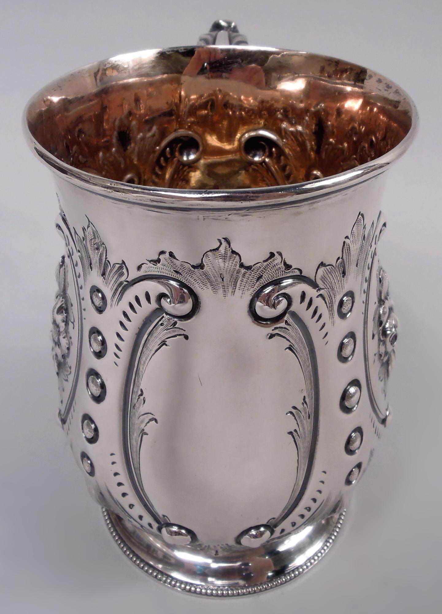 English Victorian Classical sterling silver cann, 1864. Baluster bowl with leaf-capped double-scroll handle and raised and beaded foot. Four scroll frames with leaf and bead surrounds; two inset with flowers and two vacant. Gilt interior. Fully