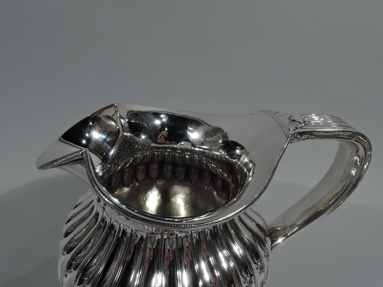 Victorian Classical sterling silver water pitcher. Made by Edward John Wells in London in 1880. Ovoid body with fluted leaf-and-dart on shoulder. Ribbed scroll-bracket handle with leaf cap and mount. Wide and round mouth with shaped spout. Cabled