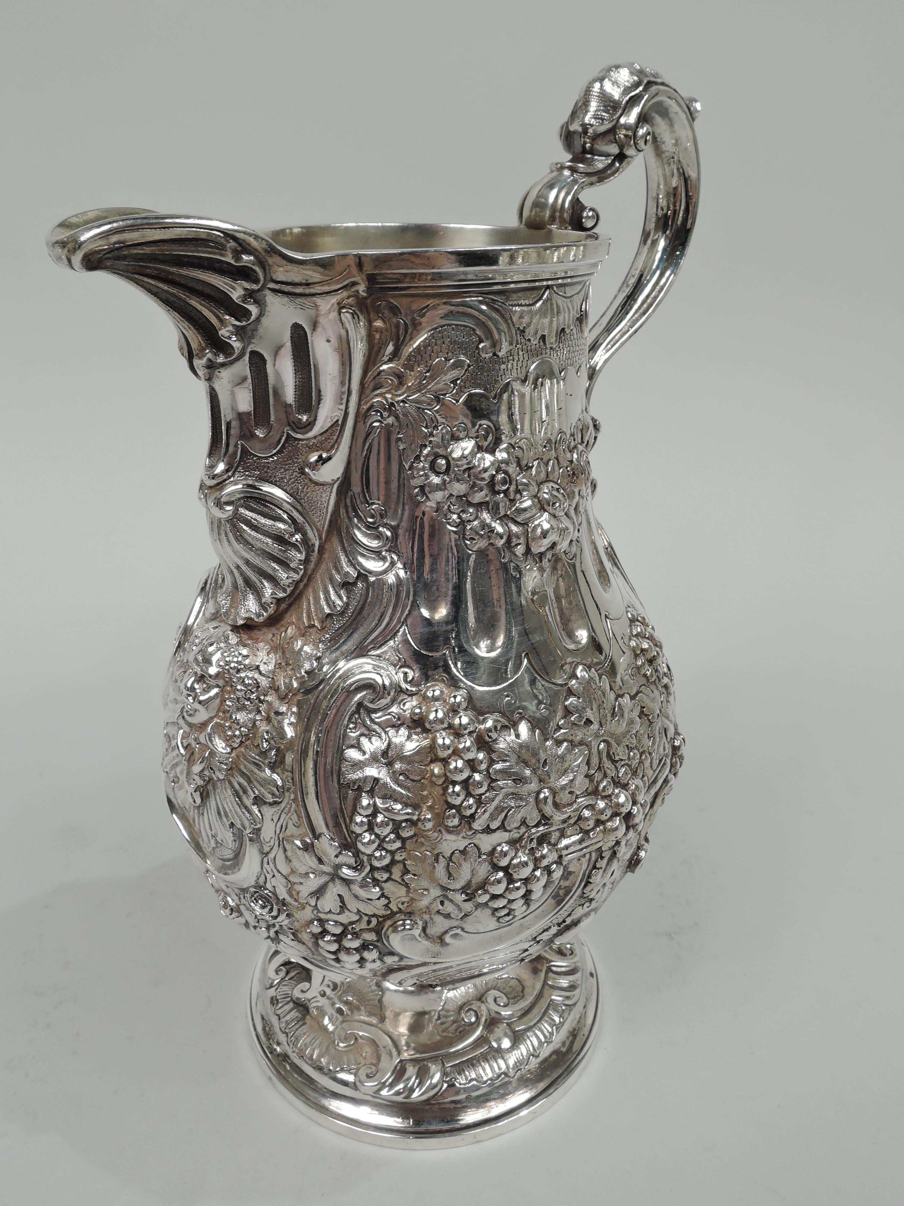 English Victorian Classical sterling silver decanter jug, 1874. Ovoid body with high-looping and leaf-capped double-scroll handle, v-form spout, and raised foot. Chased fruiting grapevine, scallop shells, and Bacchus heads. Gilt-washed interior.