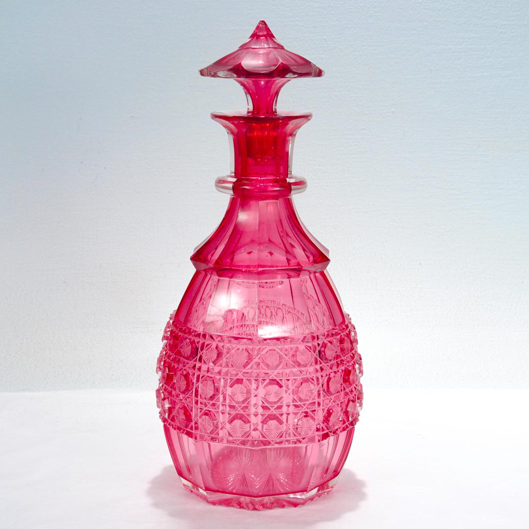 A fine antique cut glass decanter.

In cranberry cased glass.

With a single applied ring to the neck and wheel cut panels, a star cut base, and a field of finely cut body - all cut in a clear glass layer casing a cranberry interior.

With a