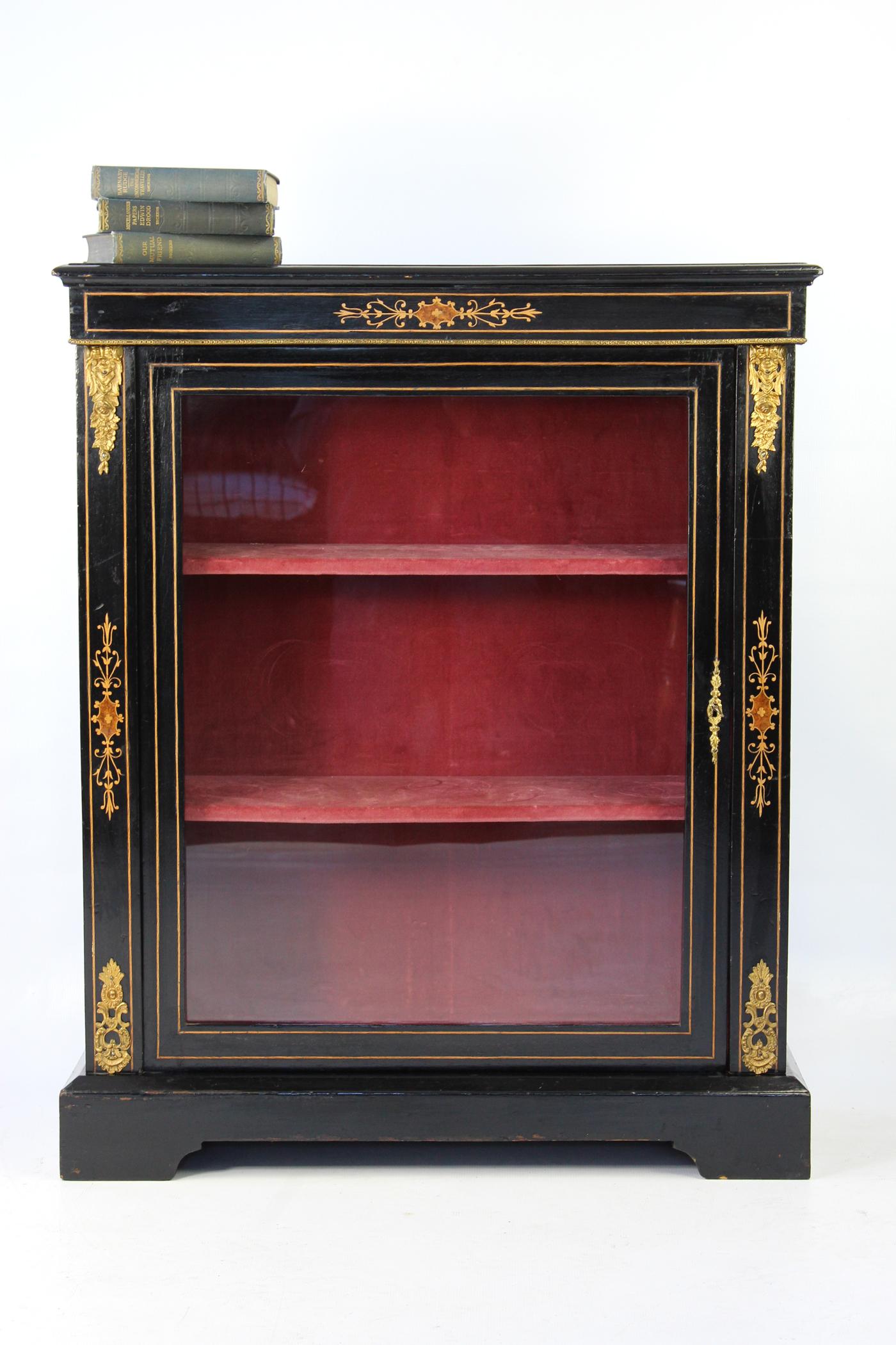 An elegant antique Victorian ebonised and marquetry pier cabinet / bookcase with lockable single glazed door. With marquetry inlaid decoration, with gilt ormolu mounts to the top and bottom corners and brass trim around the top. It comes with a
