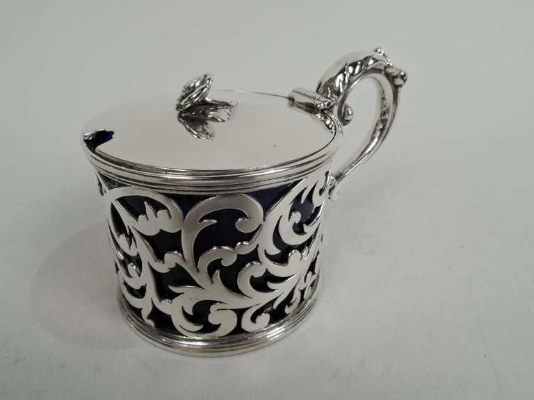 Victorian Georgian sterling silver mustard pot. Made by Samuel Hayne & Dudley Cater in London in 1838. Open scrollwork sides between reeded rims. Cover hinged with gently curved top and flower finial. Open bottom and leaf-capped double-scroll