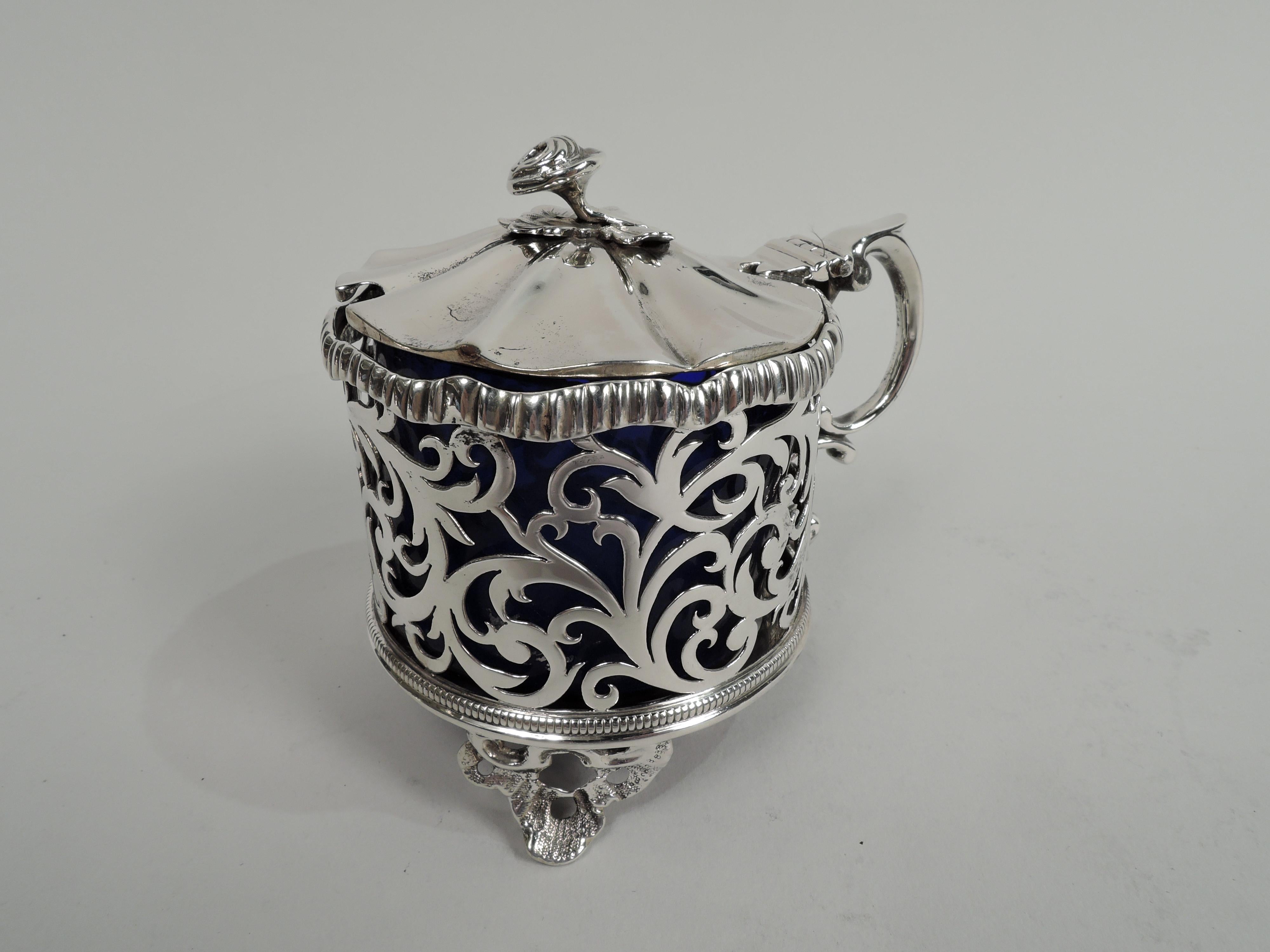 English Victorian Georgian sterling silver mustard pot, 1839. Open scrollwork sides between bead-and-reel and gadrooned rims. Cover hinged and raised with radiating flutes and leaf-mounted flower finial. Open bottom and 3 open scrolling-leaf