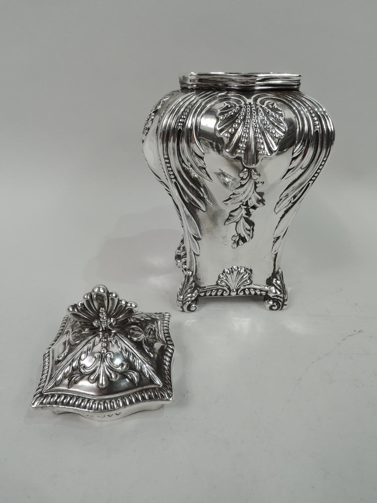 English Victorian Georgian sterling silver tea caddy, 1894. Baluster body on leaf-capped volute-scroll corner supports. Cover shaped and raised with scallop shell finial. Chased scallop shells with pendant flowers between scrolling leaf frames.
