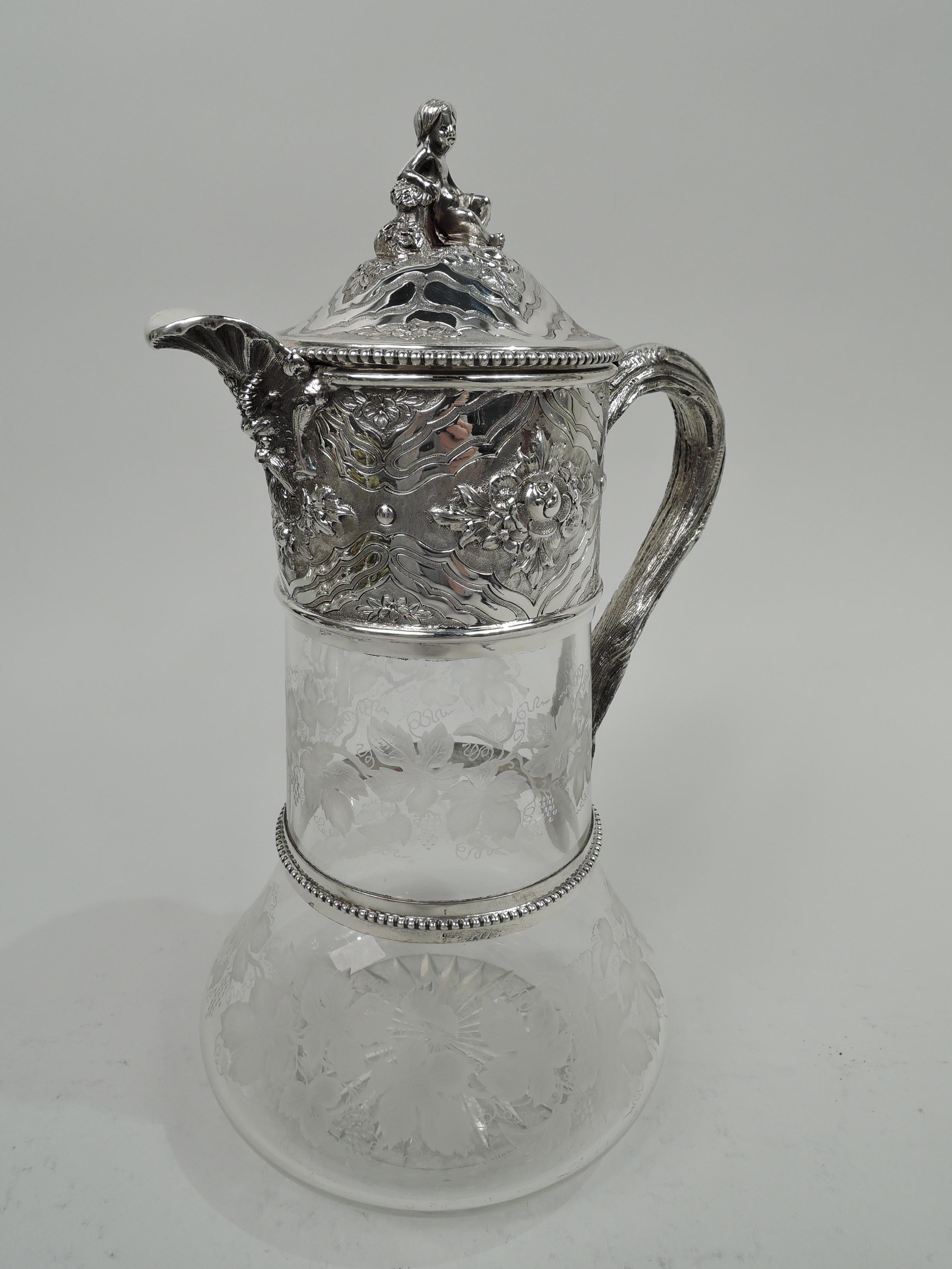 Victorian glass decanter with sterling silver mounts. Made by William & George Sissons in Sheffield in 1876. Cylindrical with spread base; etched fruiting grapevines. Sterling silver collar with branch-form scroll-handle mounted at base to beaded