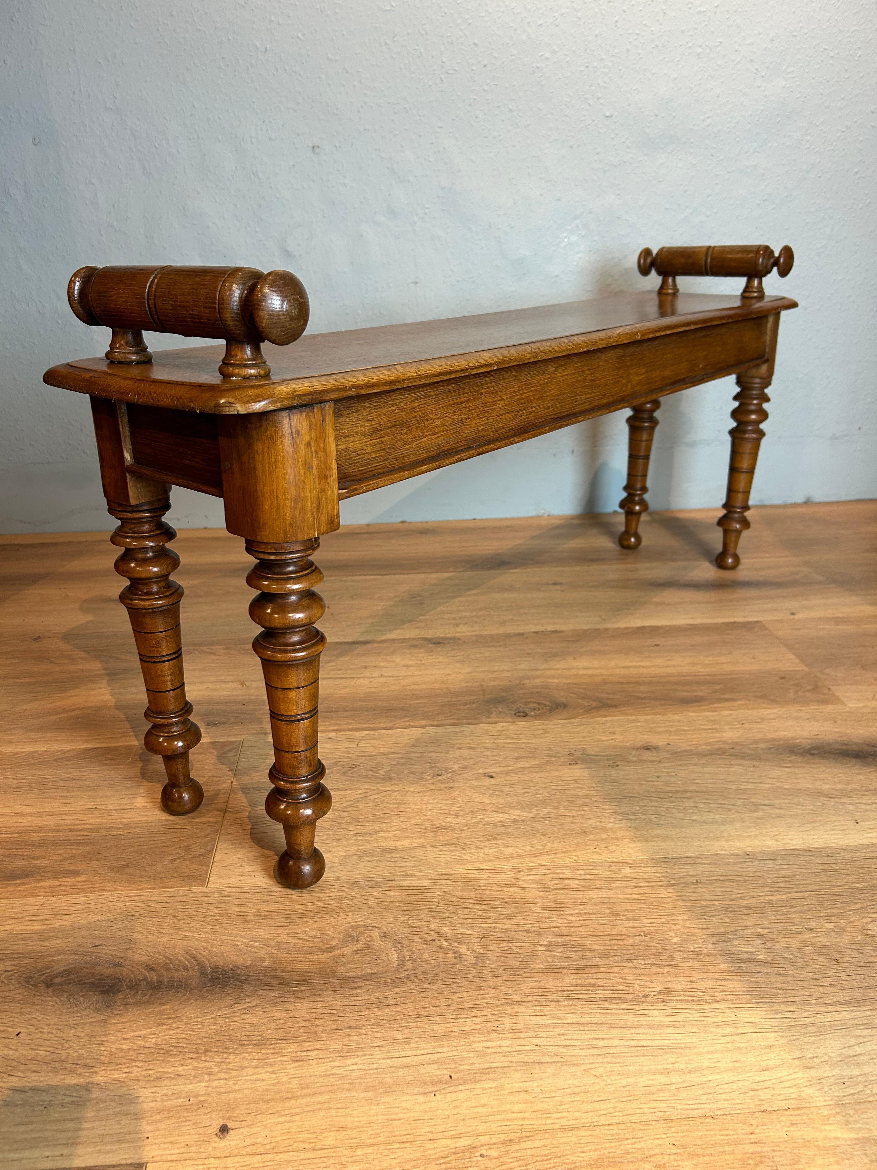 Antique English Victorian oak hall bench circa 1860 with raised bolster turned ends on a solid moulded seat resting on ornate turned legs with a pleasant honey colour.