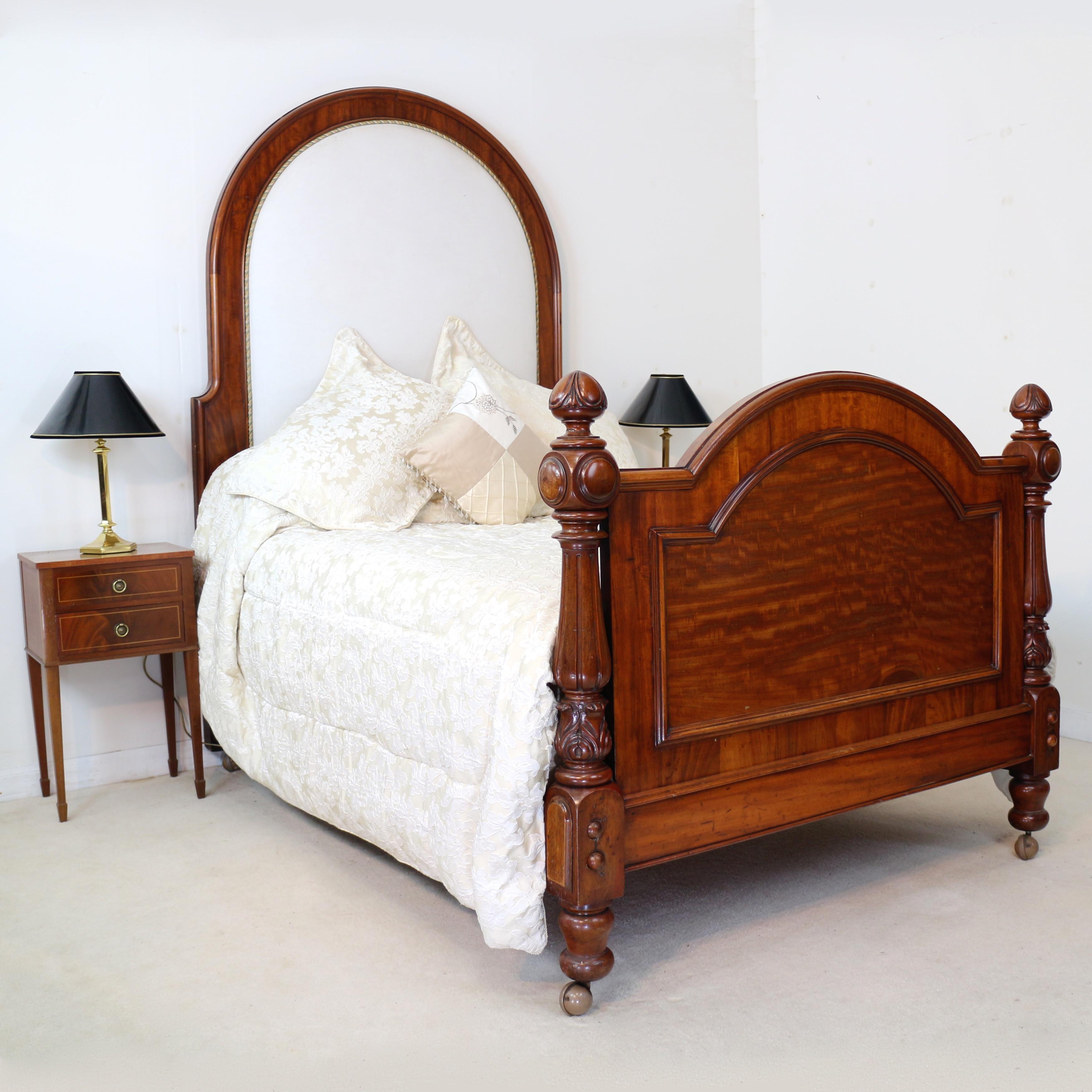 A handsome Victorian mahogany and upholstered double bed dating to circa 1880. With a tall half tester size arched padded and upholstered headboard and two acanthus carved and fluted columns flanking the moulded panelled upholstered footboard, it