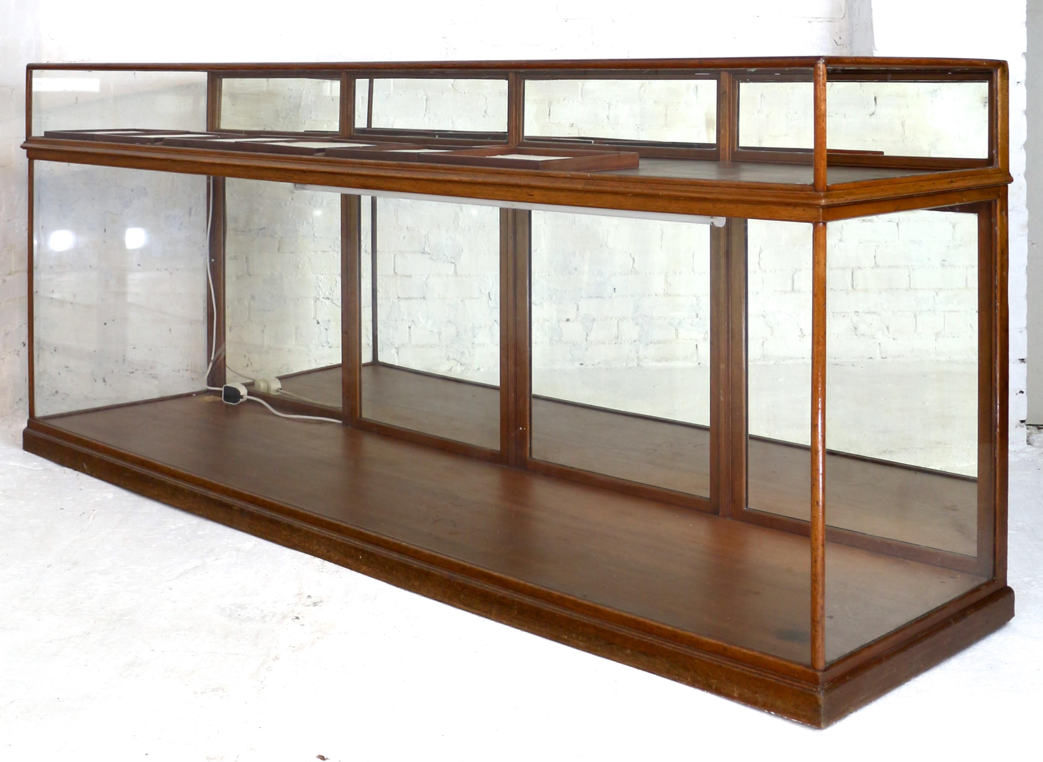 A good quality Victorian jewellery shop counter or cabinet, with a narrow mahogany frame and toughened glass sides the top has four mirrored lockable flap doors which provide access to the top, and four doors to the base with brass catches. With