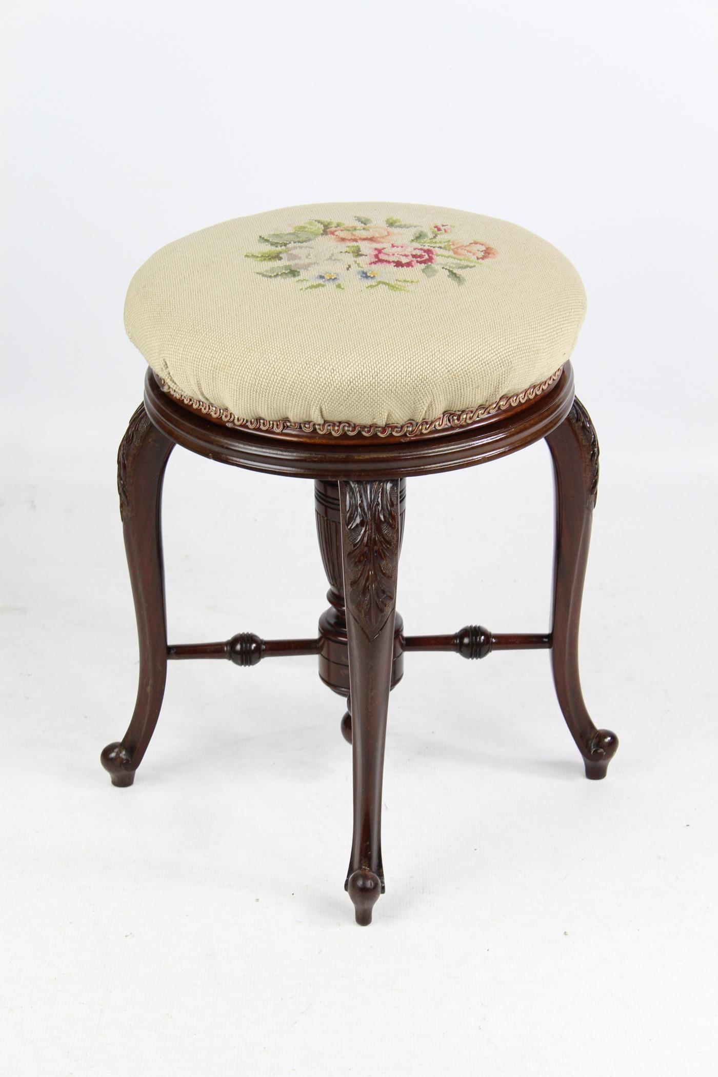 An elegant antique late Victorian mahogany revolving piano stool, stamped J Fitter Birmingham dating from circa 1900. With an oval stuff over top upholstered in floral gros point which raises up on a brass thread. It stands on four acanthus carved