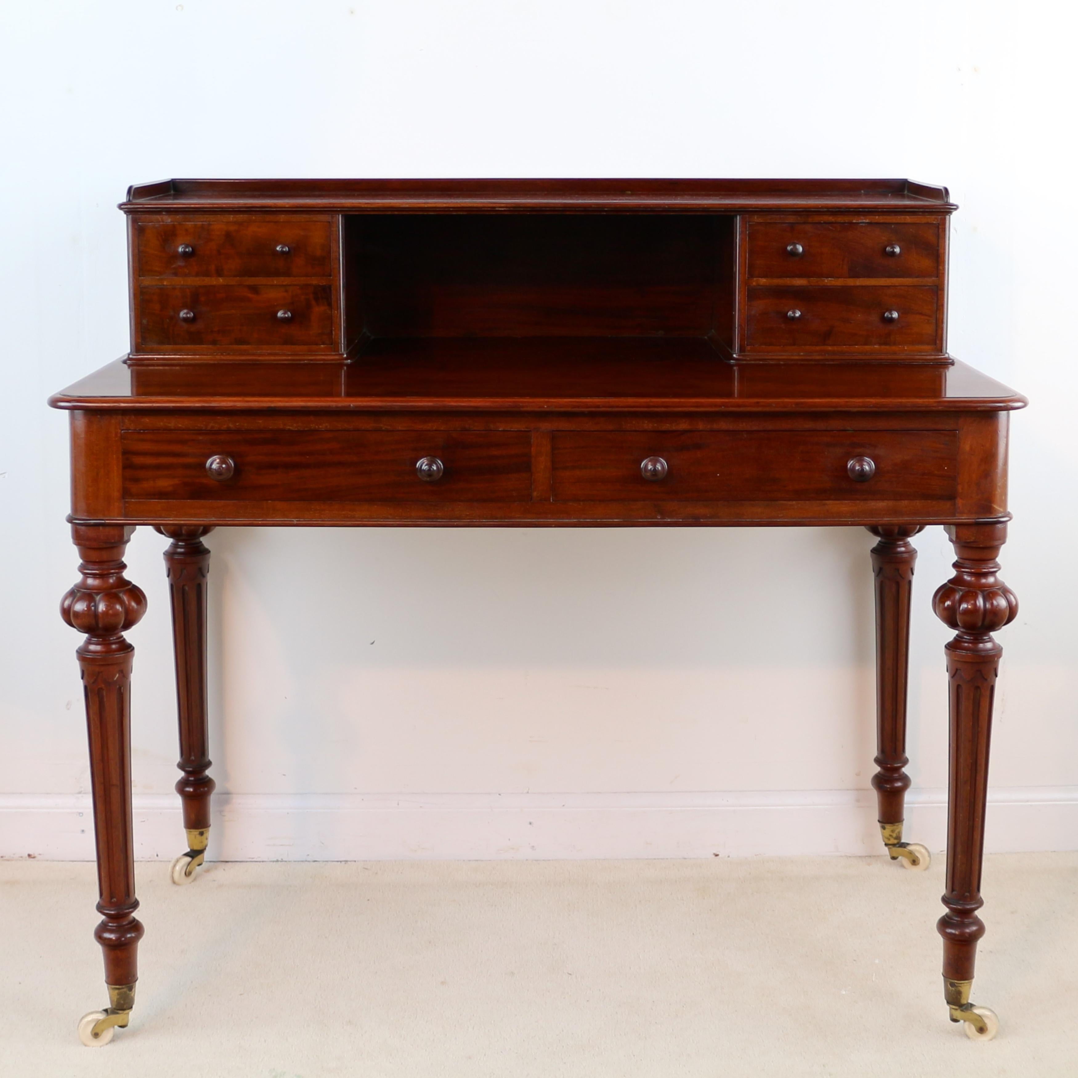 A handsome Victorian mahogany writing table or desk by Heal’s of London. This example features a raised back with galleried shelf and four small drawers and two further deep drawers to the table, standing on attractive turned legs with bold reeding