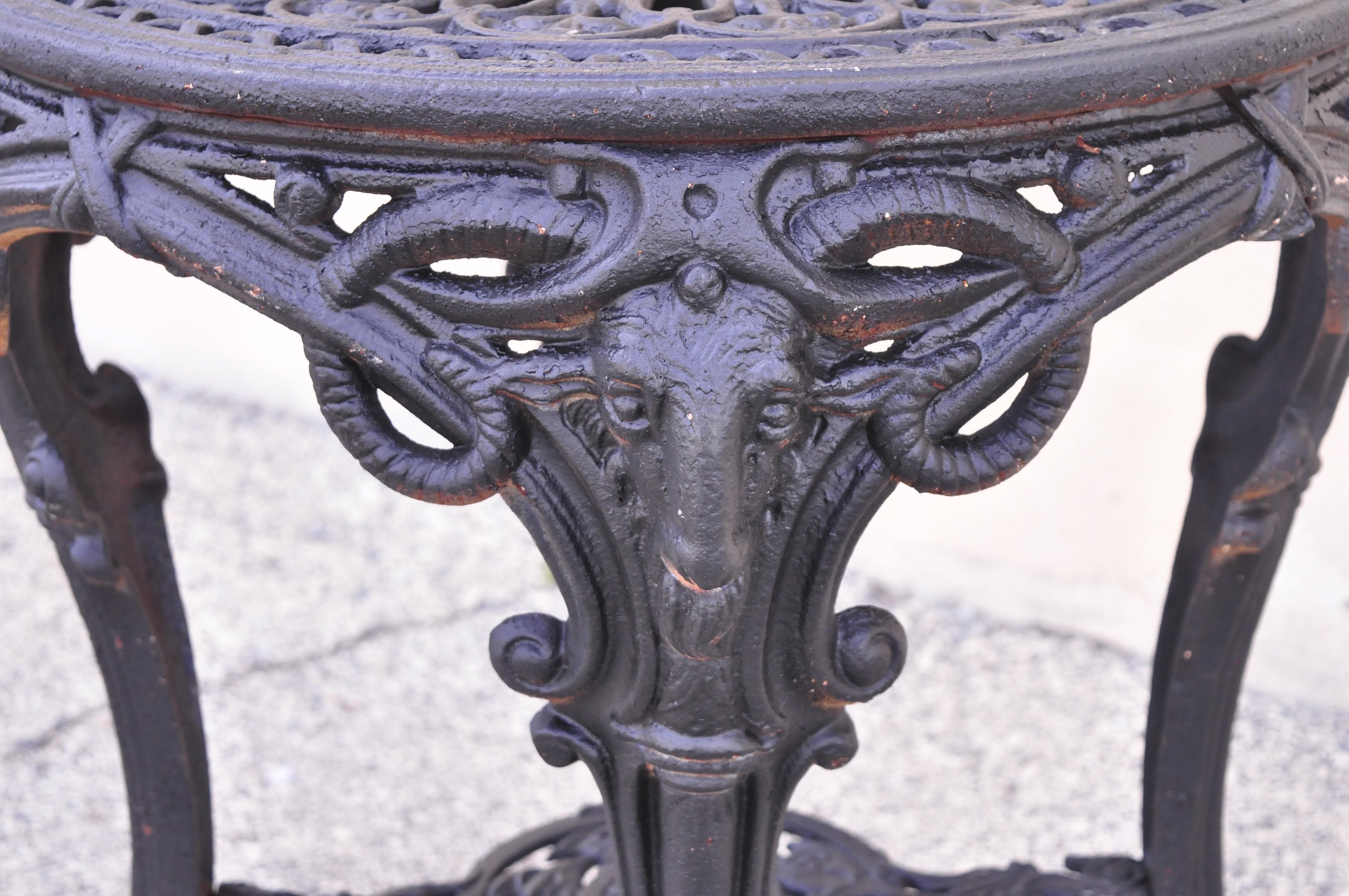 Antique English Victorian Regency cast iron round pub center table with rams heads. Item features rams heads and hoof feet, pierced design to top and lower shelf, black painted finish, cast iron construction, very nice antique item. Approx. 80 lbs.