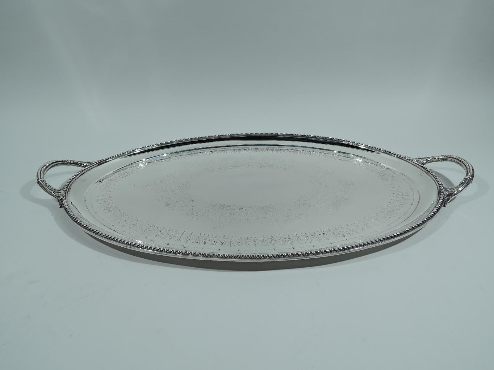 Victorian Regency sterling silver tea tray. Made by Walter & John Barnard in 1881. Oval with beaded rim and leaf-mounted and beaded c-scroll end handles. Well has central oval cartouche (vacant) with leaf-and-dart border and multi-foil surround. Two