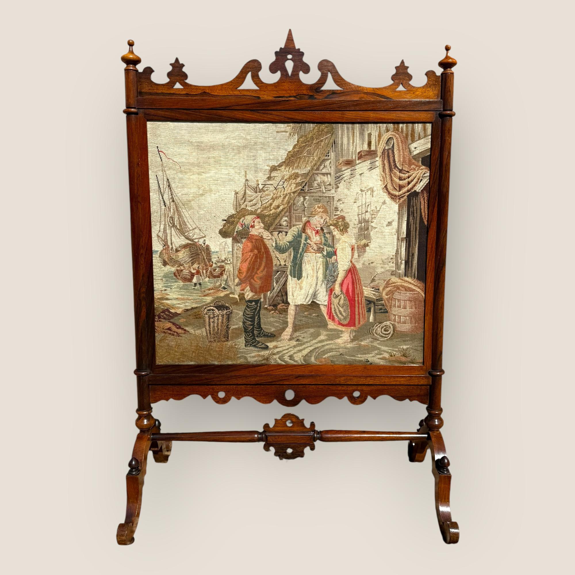 Ecco un antico parafuoco inglese di epoca medio-vittoriana (1850-1870) in palissandro e agugliato. Il pannello con il ricamo raffigura una scena di porto con persone che parlano, barche a vela e case di paglia sullo sfondo. La parte superiore delle