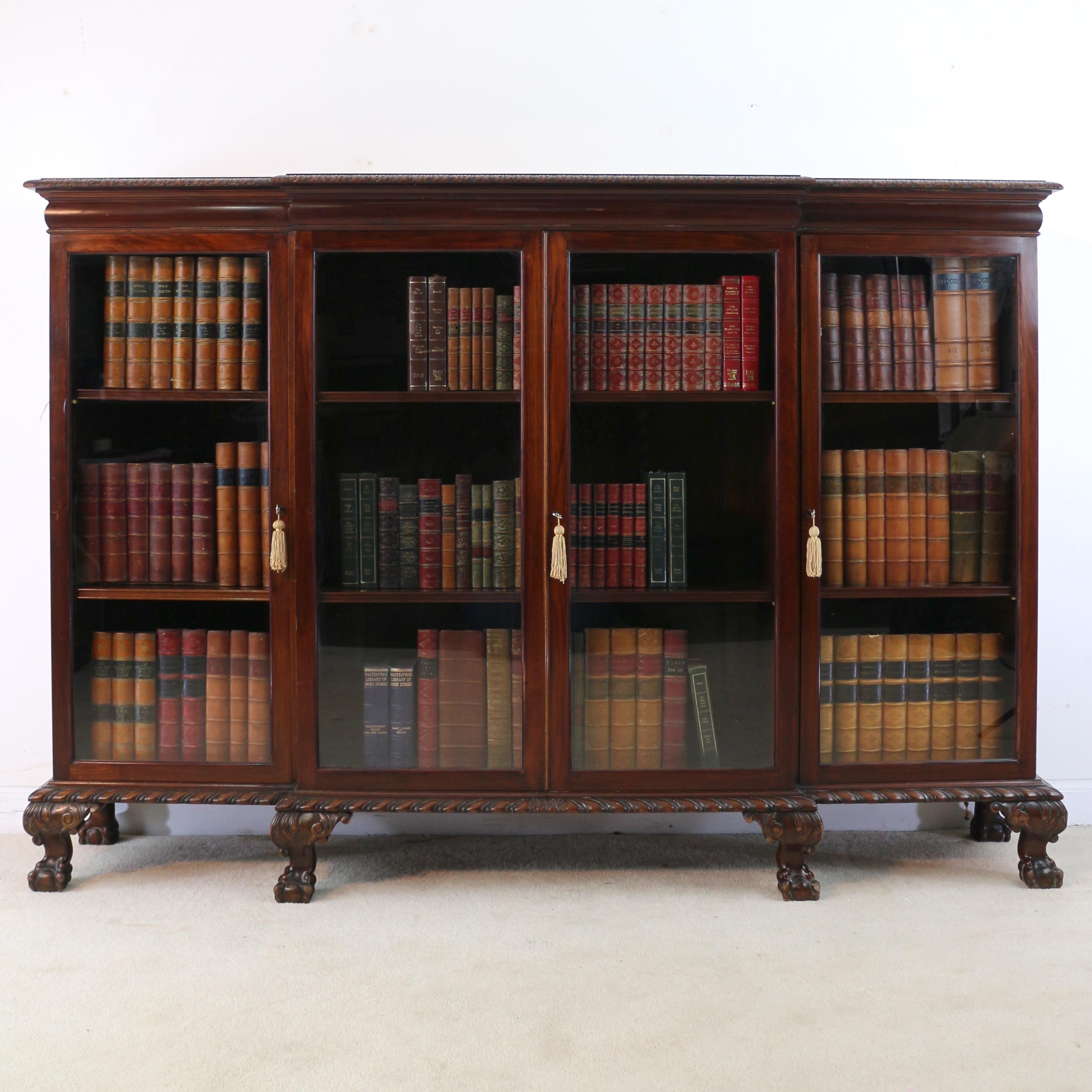 An attractive late 19th century solid mahogany four door breakfront dwarf bookcase / cabinet in the Chippendale style. The rectangular breakfront top with a leaf carved edge above a swelled frieze, the four glazed doors below with working locks and
