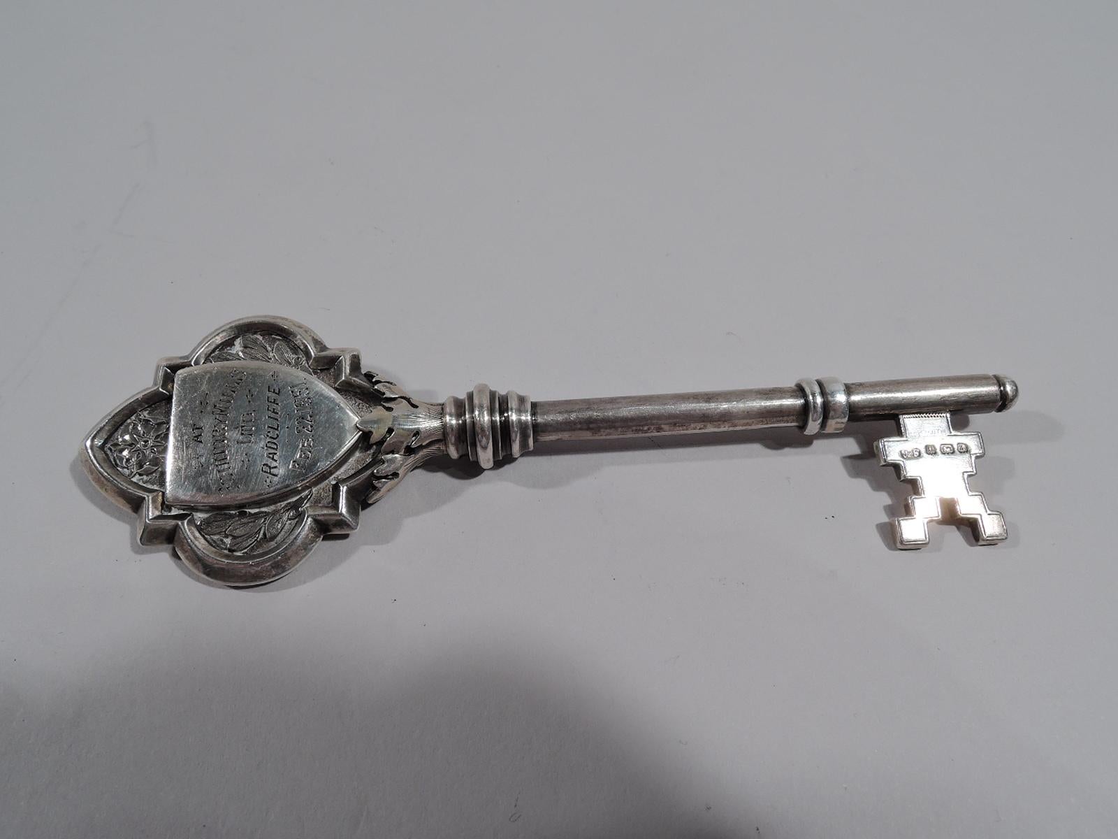 Victorian sterling silver ceremonial key. Made by James Fenton & Co. in Birmingham in 1900. Shaped and curvilinear double-sided head with chased leaves and flowers and armorial cartouches; fretwork bit. Engraved presentation. On front cartouche: