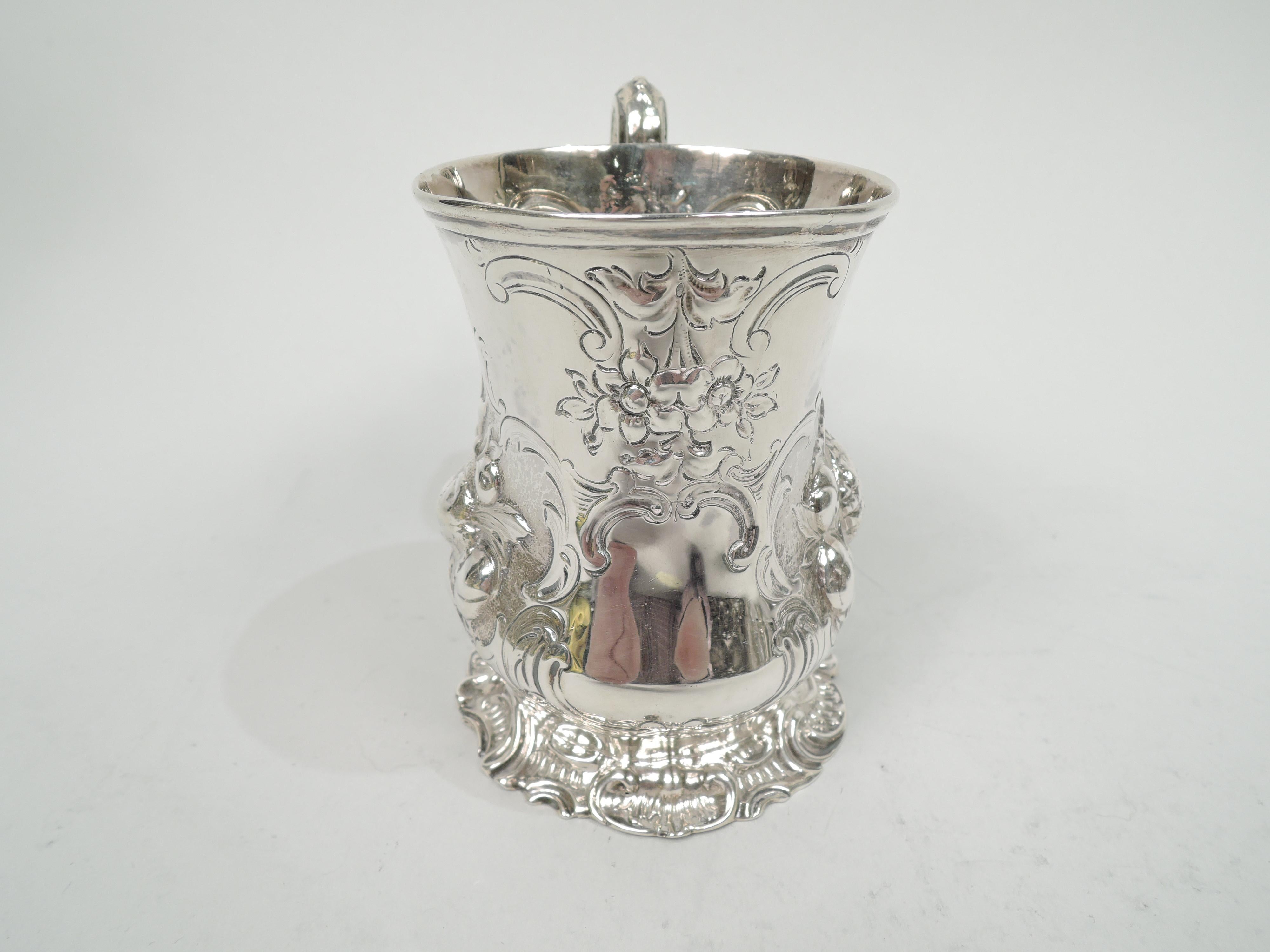 Victorian sterling silver baby cup. Made by George John Richards in London in 1853. Baluster bowl with leaf-capped double-scroll handle and scrolled skirted foot. Embossed vegetation clusters in engraved leafing scroll frames; a third frame vacant.